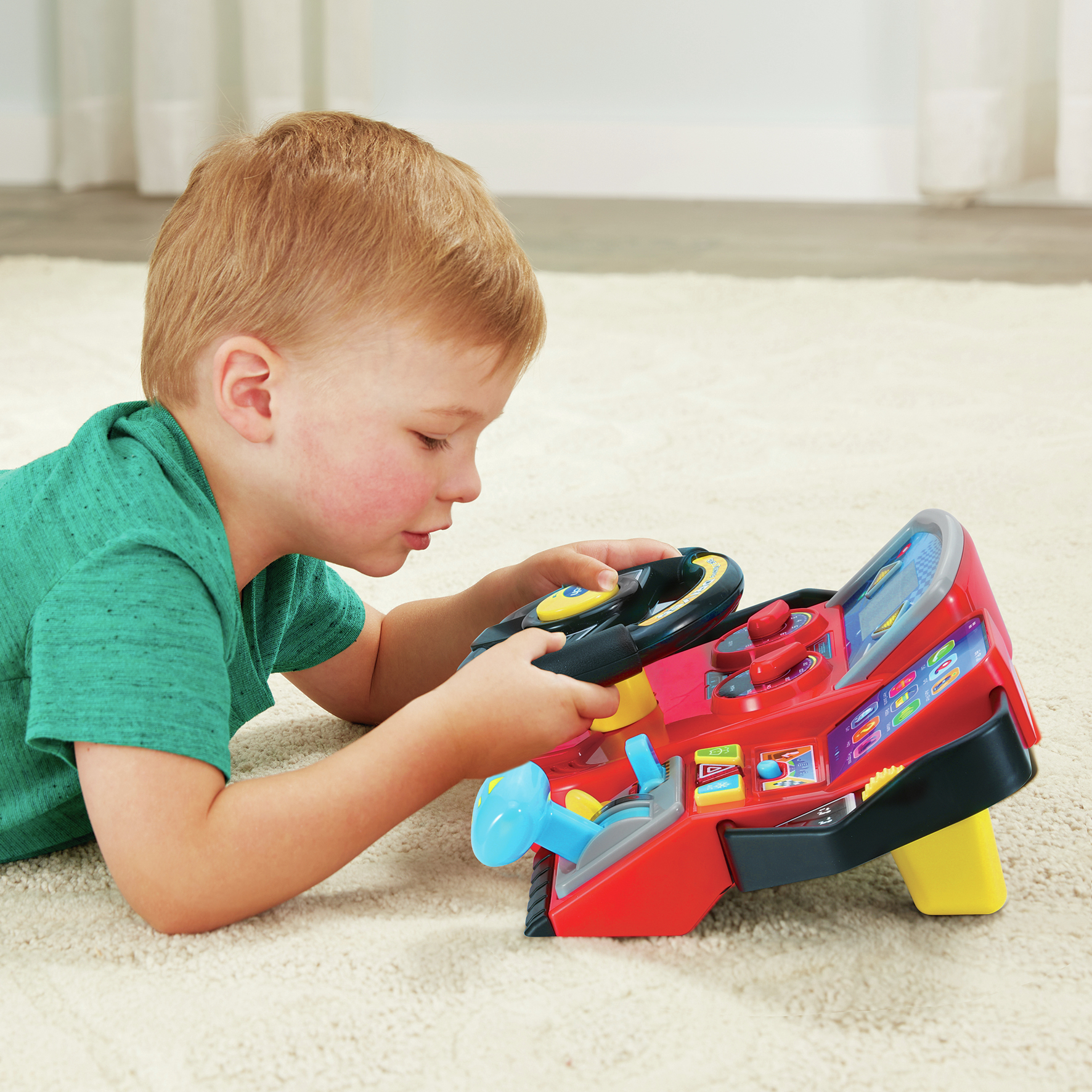 Un ragazzo che gioca con una console per auto giocattolo rossa, sdraiato su un tappeto color crema.
