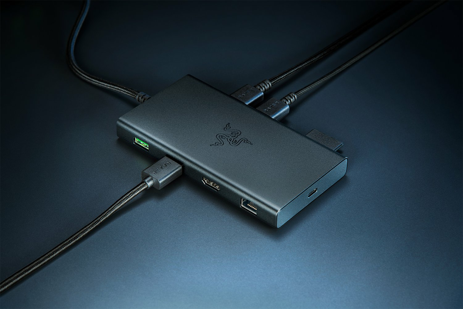 Ein schwarzer Razer USB-Hub mit mehreren Anschlüssen, der an mehrere Geräte angeschlossen ist, auf einer dunkelblauen Oberfläche.