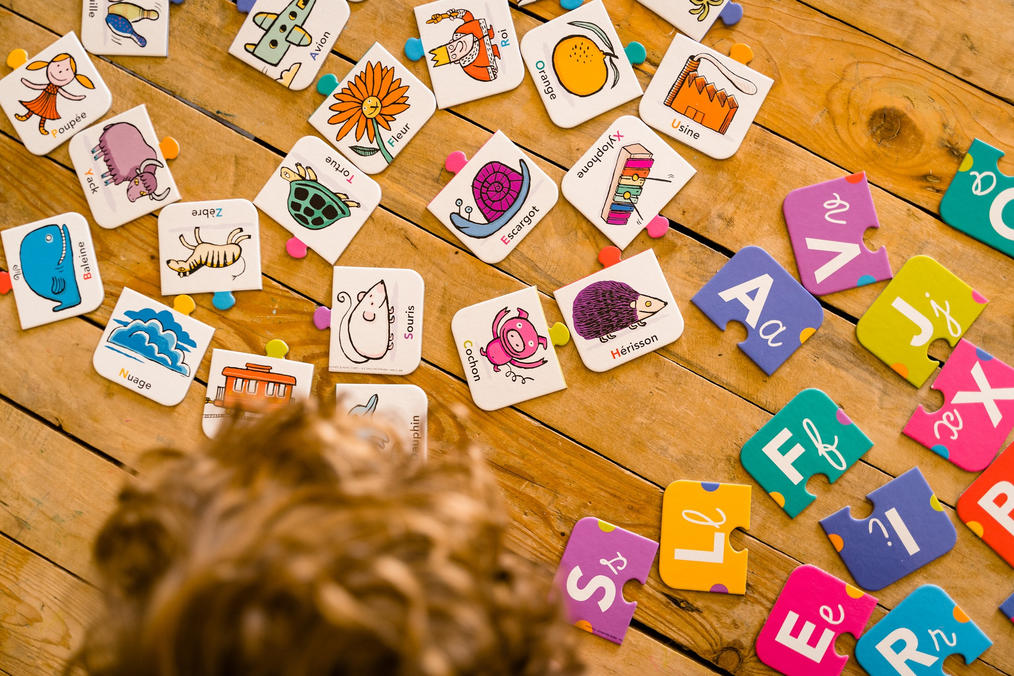 Holztisch mit mehreren Puzzleteilen. Bunte Buchstaben- und Tierpuzzles sind verstreut.