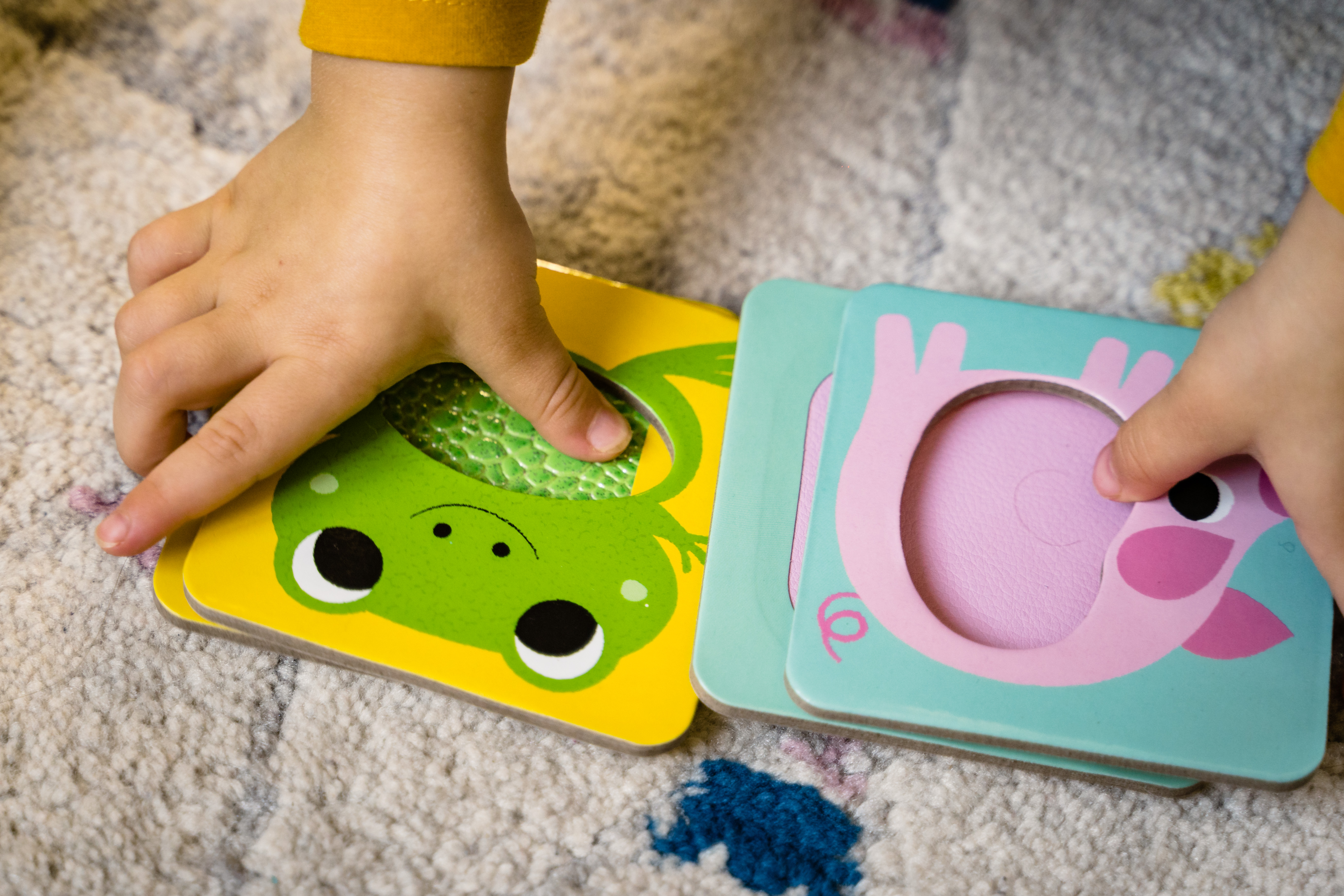 Kind spielt mit Puzzleteilen mit Tieren. Grüner Frosch und rosa Schwein sind sichtbar.