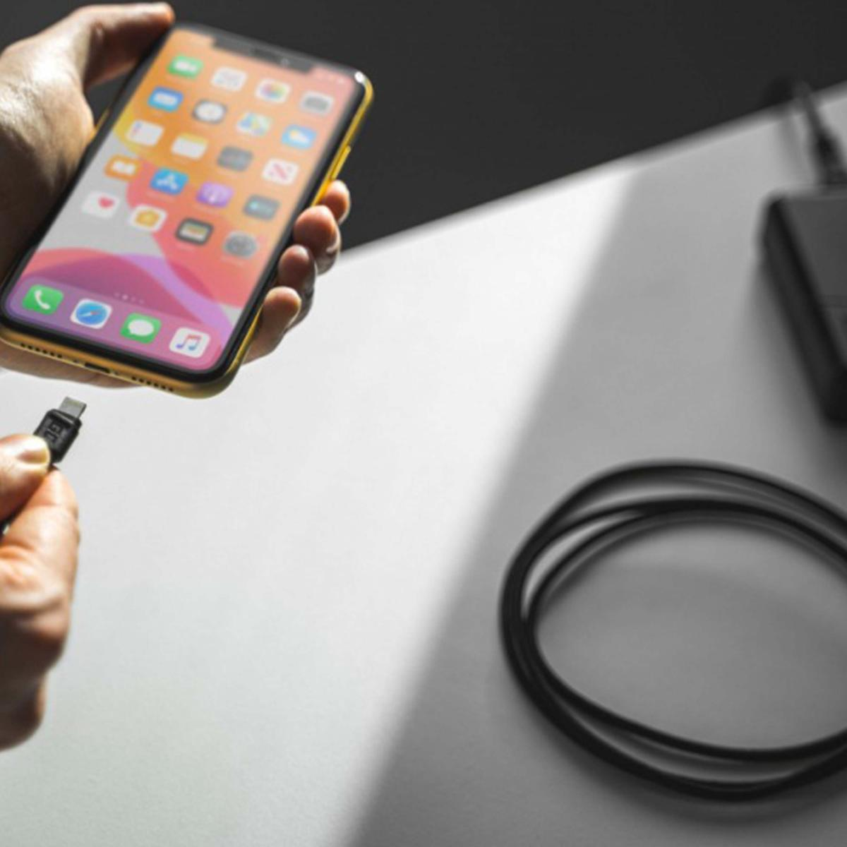 Mano che tiene un iPhone dorato con un cavo in procinto di essere collegato. Cavo di ricarica nero e caricatore nero visibili.