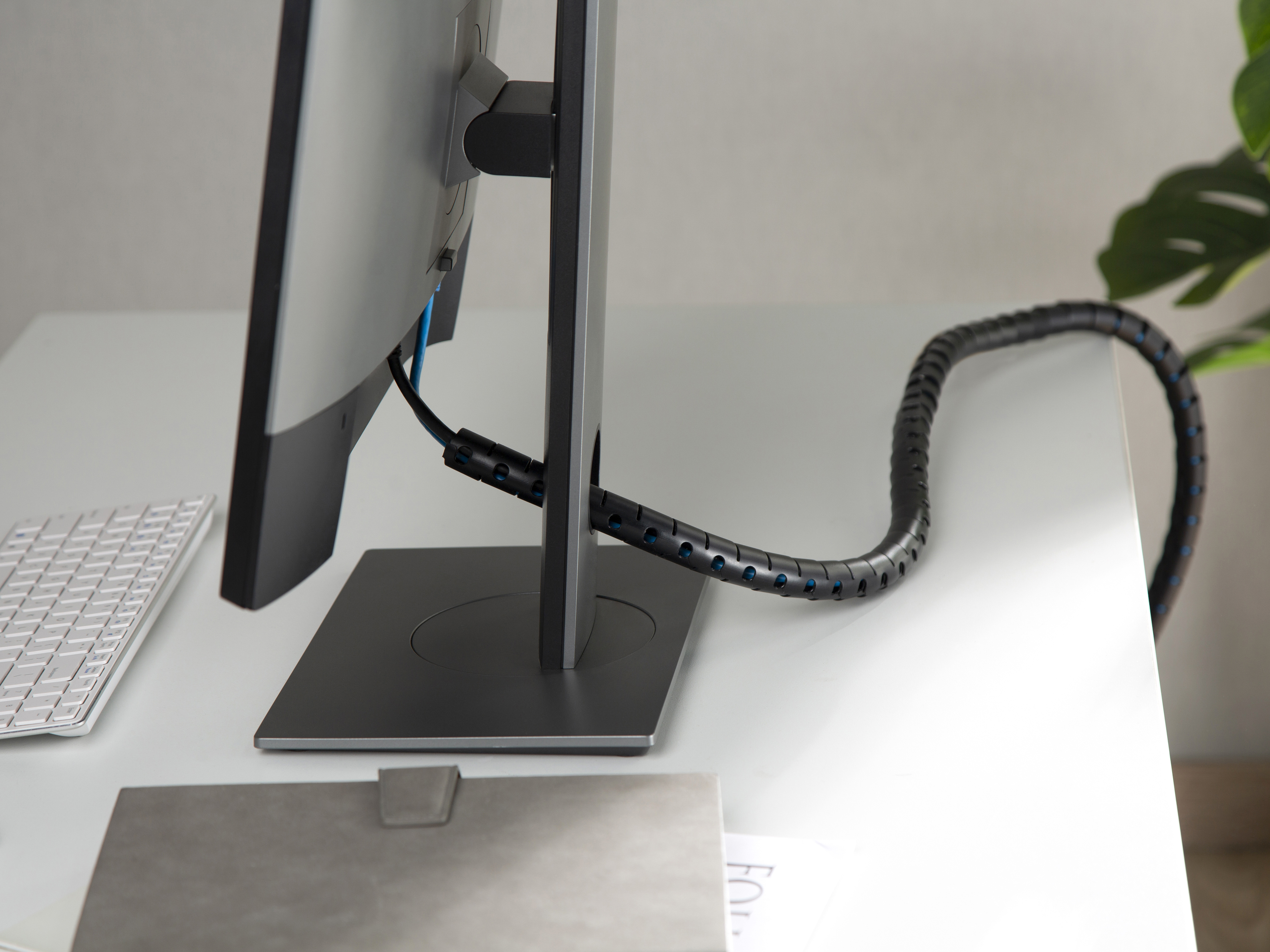 Ein Computermonitor und eine weiße Tastatur mit einem schwarzen Kabelorganisator auf einem weißen Schreibtisch.