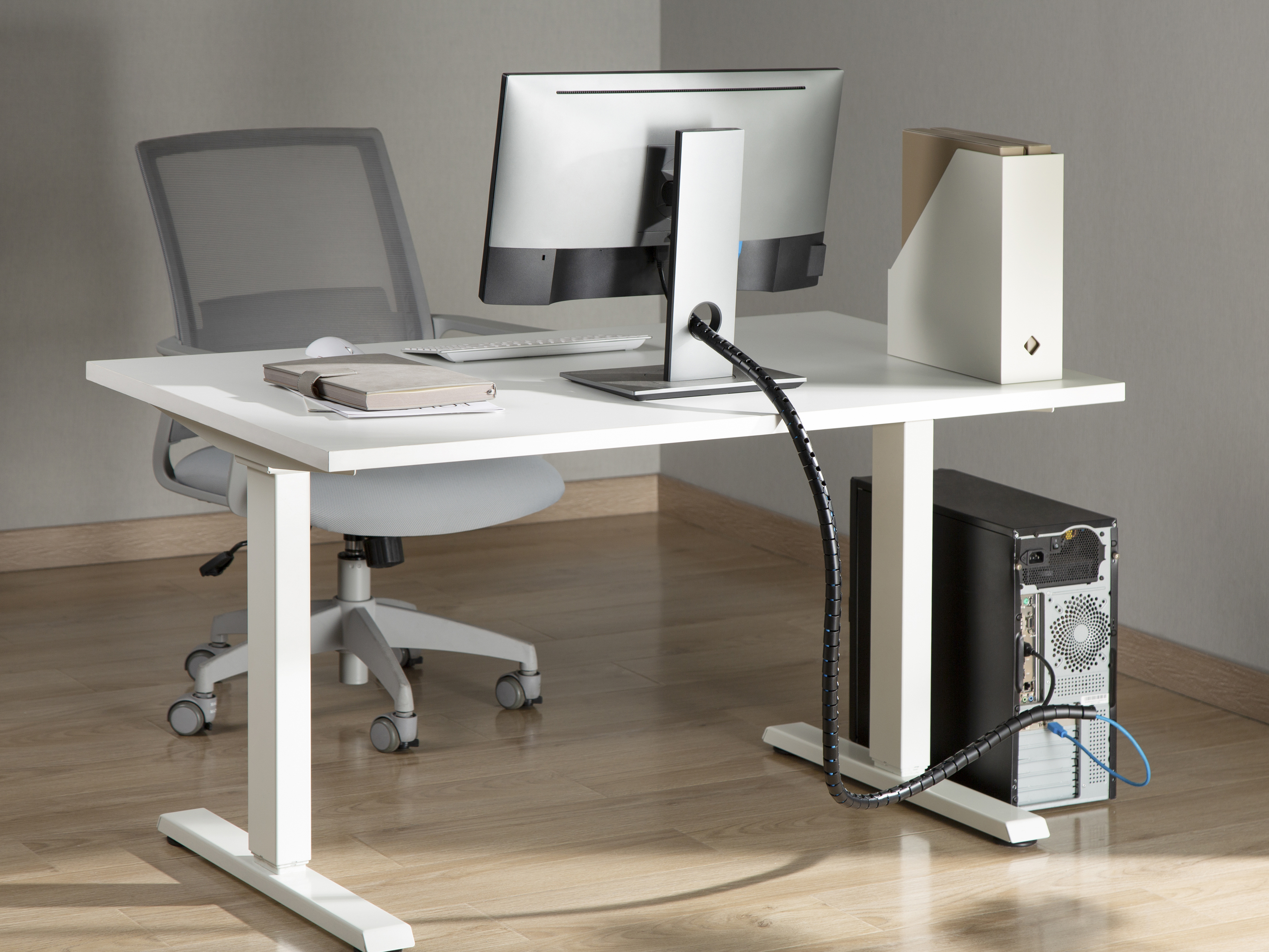 Ein weißer Schreibtisch mit Monitor, Tastatur und schwarzem Tower. Ein Netzstuhl steht daneben.