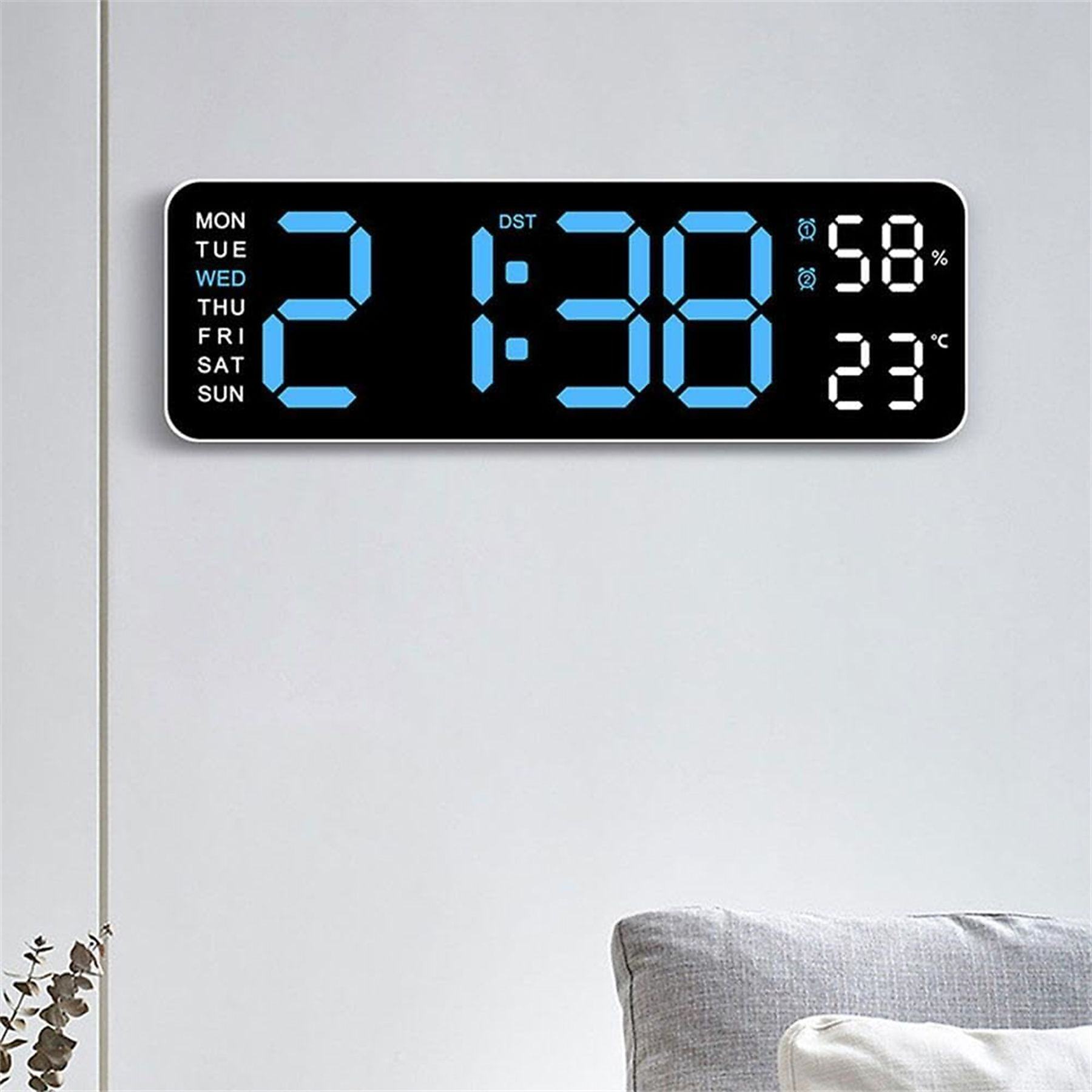 Eine schwarze Digitaluhr zeigt die Uhrzeit und das Datum vor einer weißen Wand an. Die Uhrzeit ist 21:38.