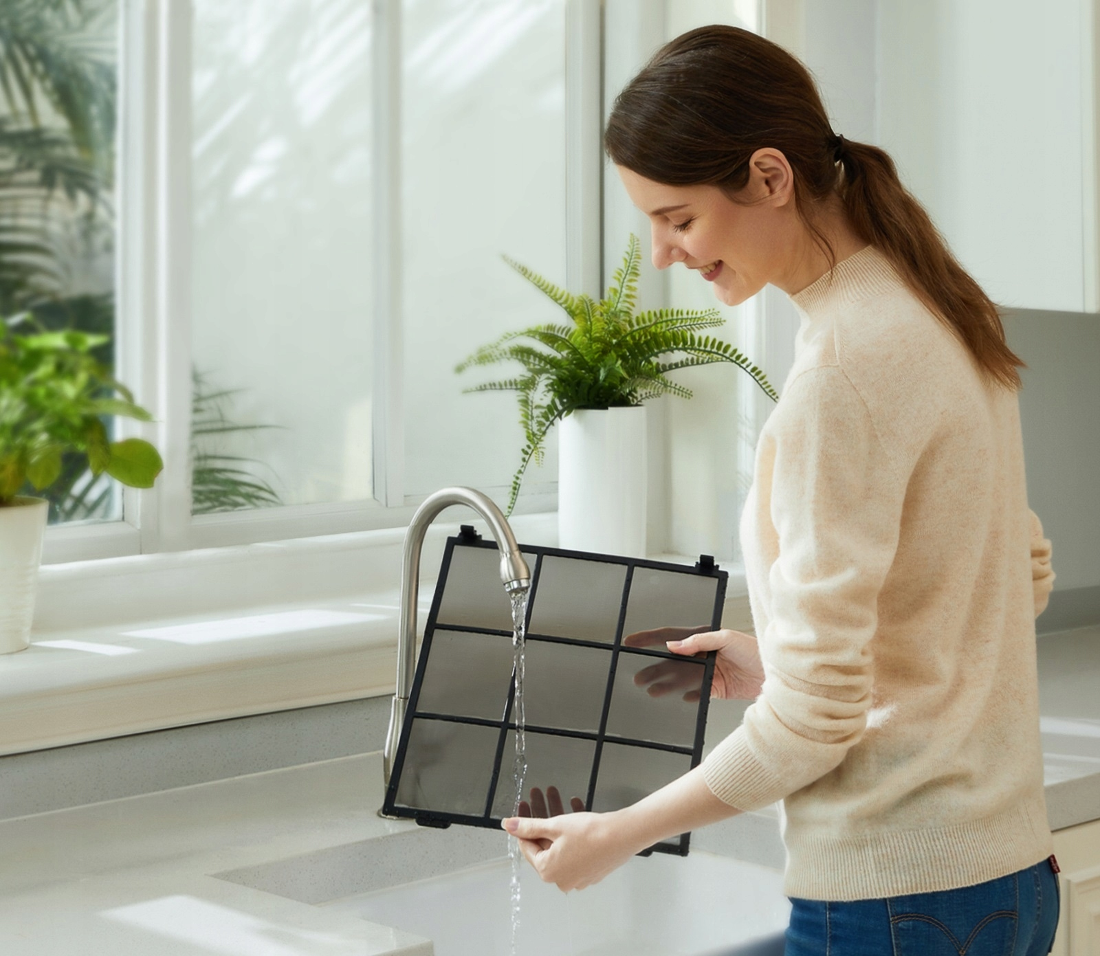 Kobieta myjąca filtr powietrza pod kranem w kuchni.