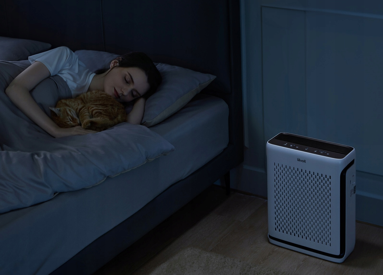 Kobieta śpiąca w łóżku z kotem i oczyszczaczem powietrza obok łóżka.
