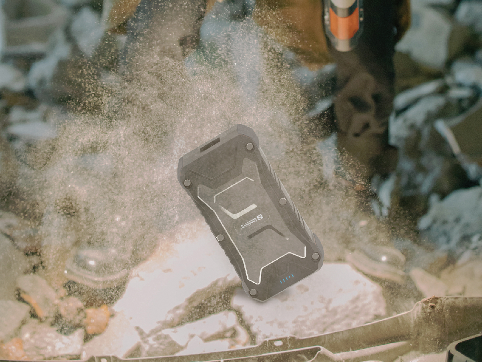 Une batterie externe noire et robuste tombe, avec de la poussière, dans un environnement extérieur.