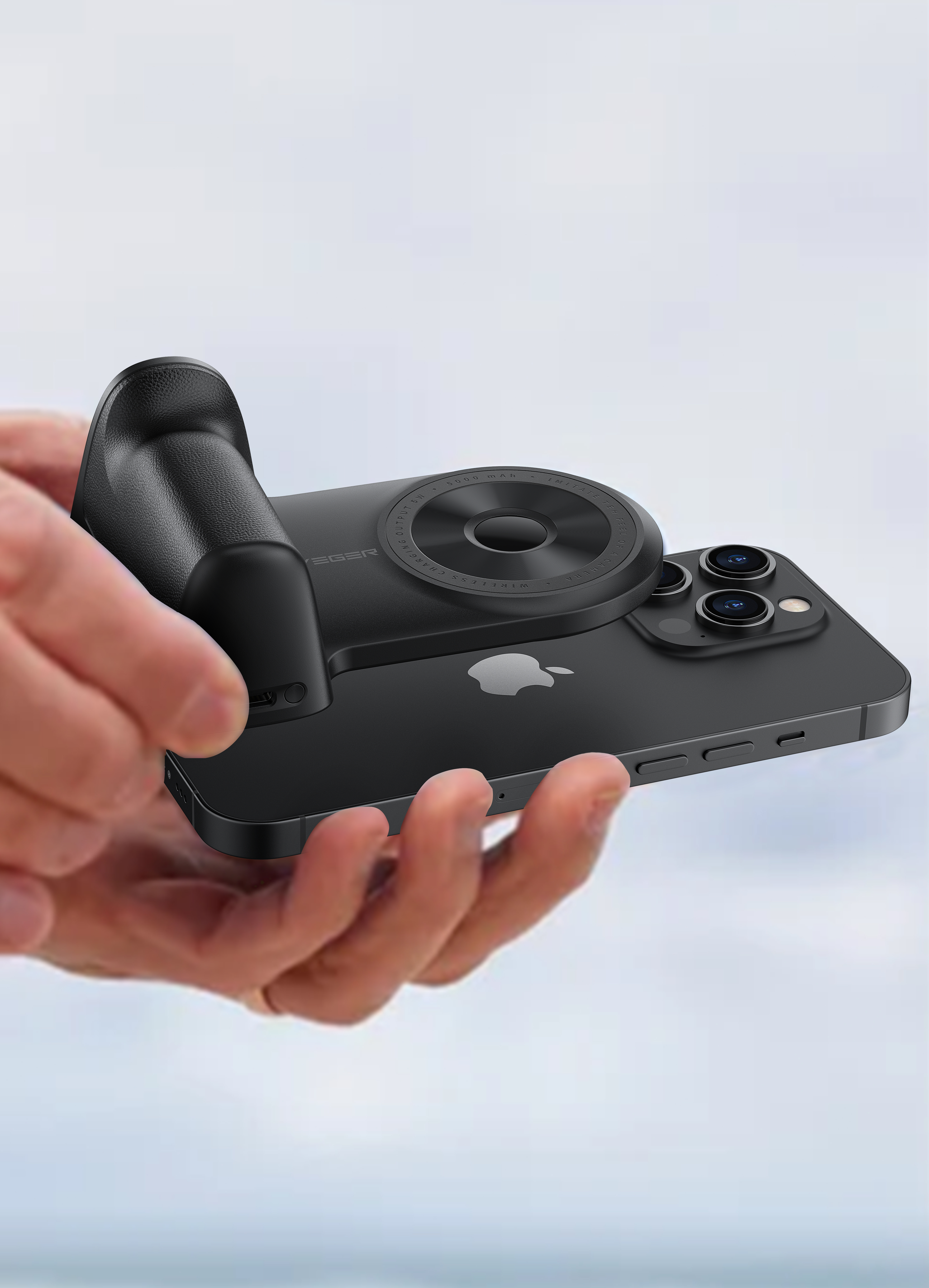 Una mano tiene un telefono nero con un accessorio per fotocamera. Lo sfondo è sfocato.