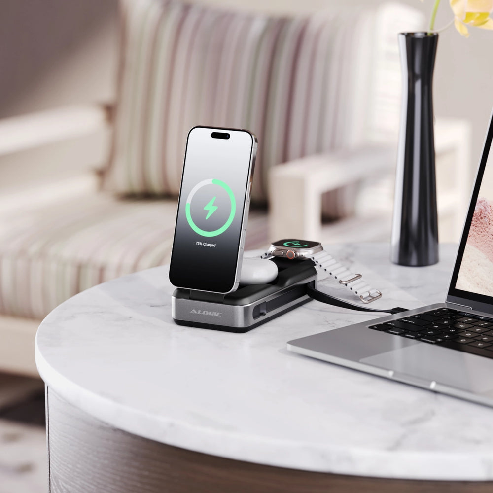 Una estación de carga moderna con teléfono, reloj y auriculares, sobre una mesa de mármol con portátil y florero.