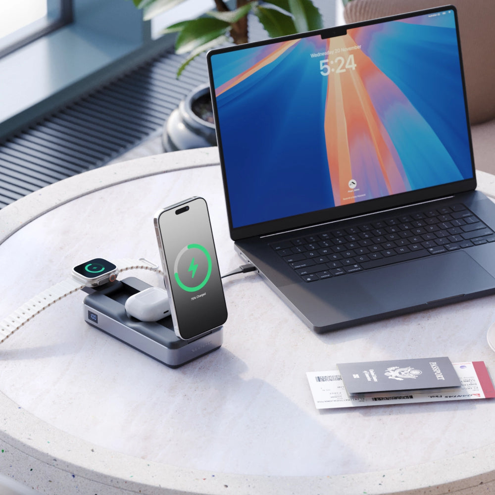 Un escritorio con una computadora portátil, un teléfono, un reloj y auriculares, todos conectados a una estación de carga.