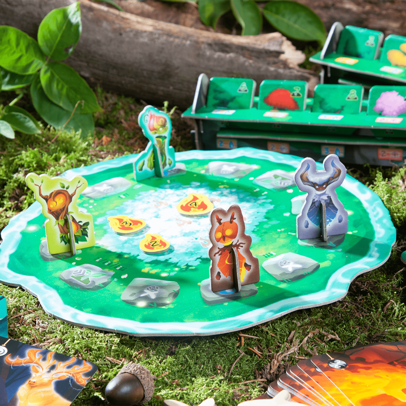 Ein Brettspiel mit Spielsteinen auf einer grünen Matte, umgeben von Moos. Figuren und Spielsteine sind sichtbar.