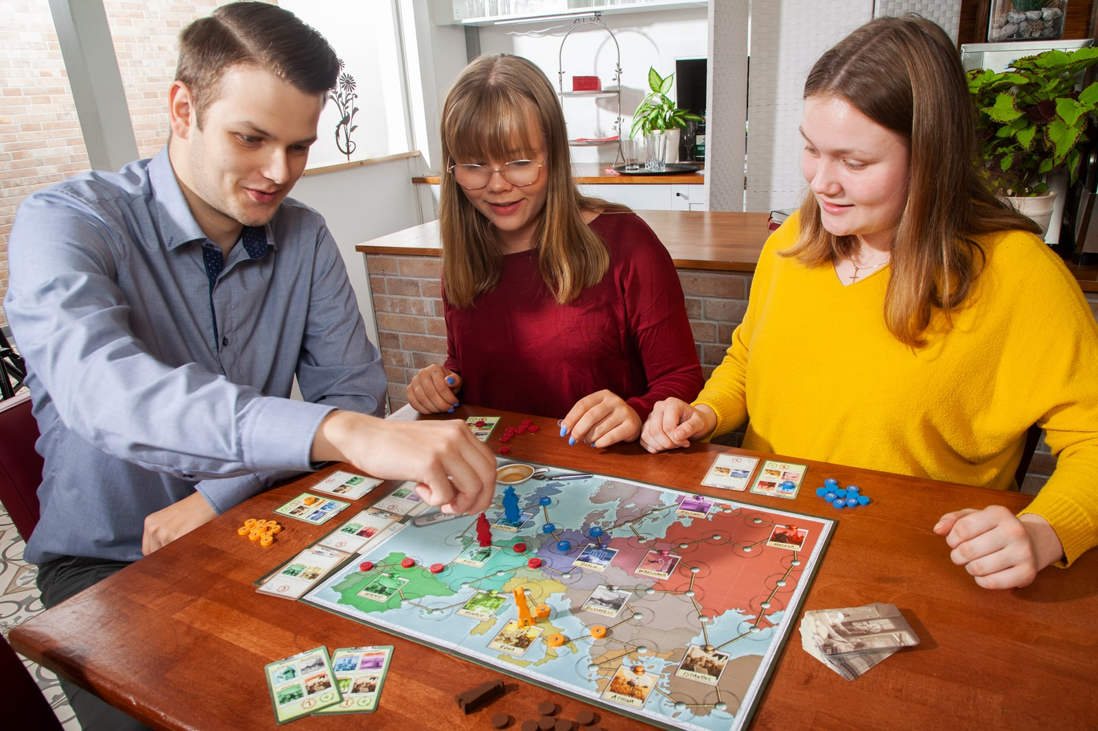 Drei Personen spielen ein Brettspiel und zeigen auf das Spielbrett mit Karten.