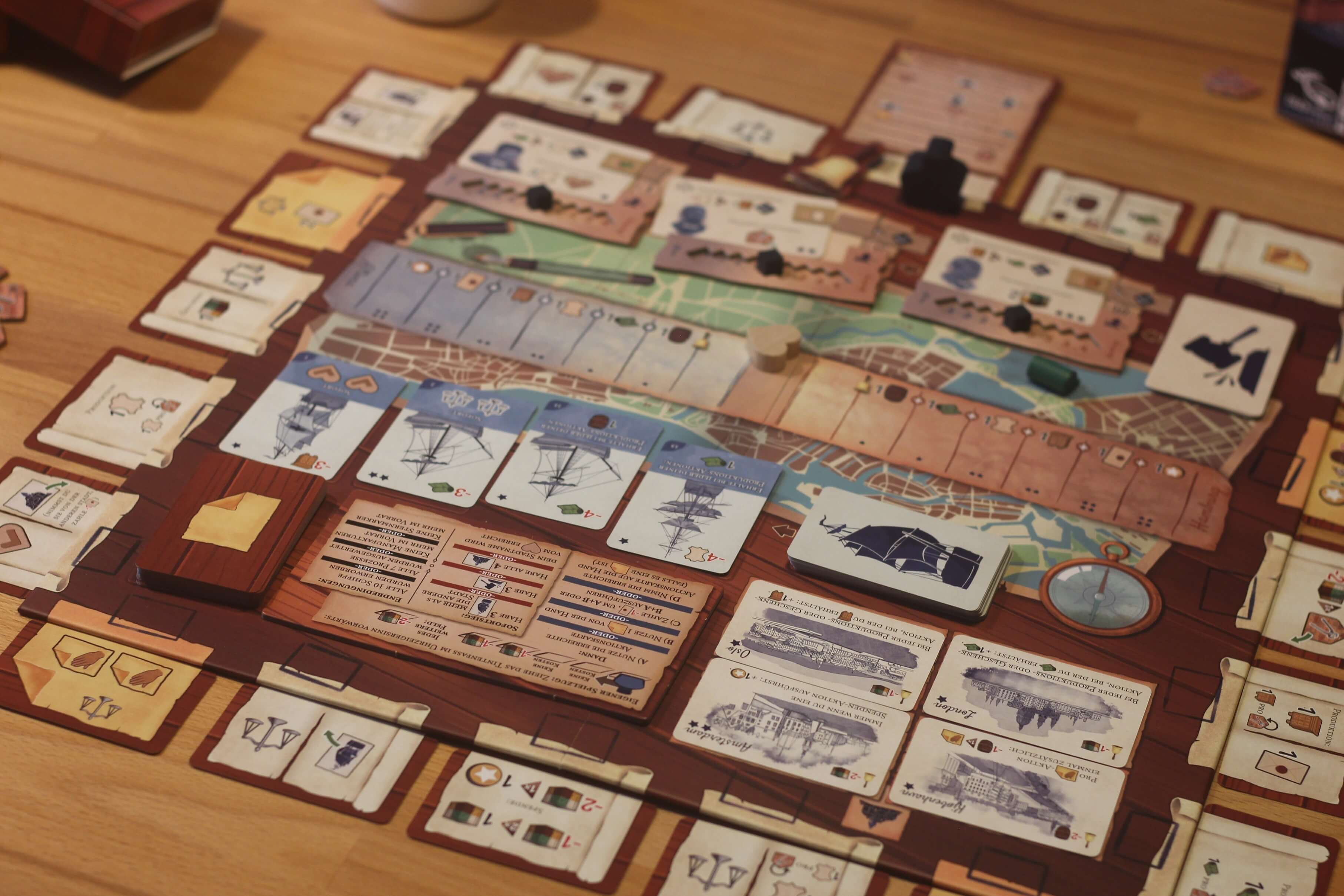 Gioco da tavolo con varie carte e pezzi. Il gioco è allestito su un tavolo di legno.