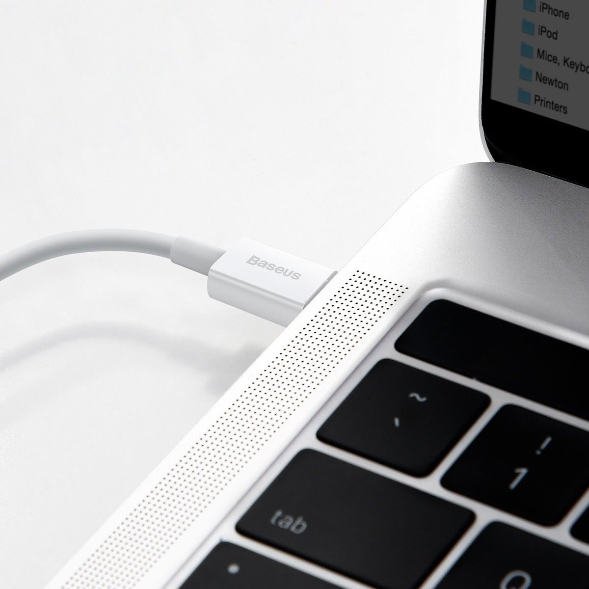 Primo piano di un cavo USB-C bianco collegato a un laptop argentato. La tastiera del laptop è visibile e lo sfondo è bianco.