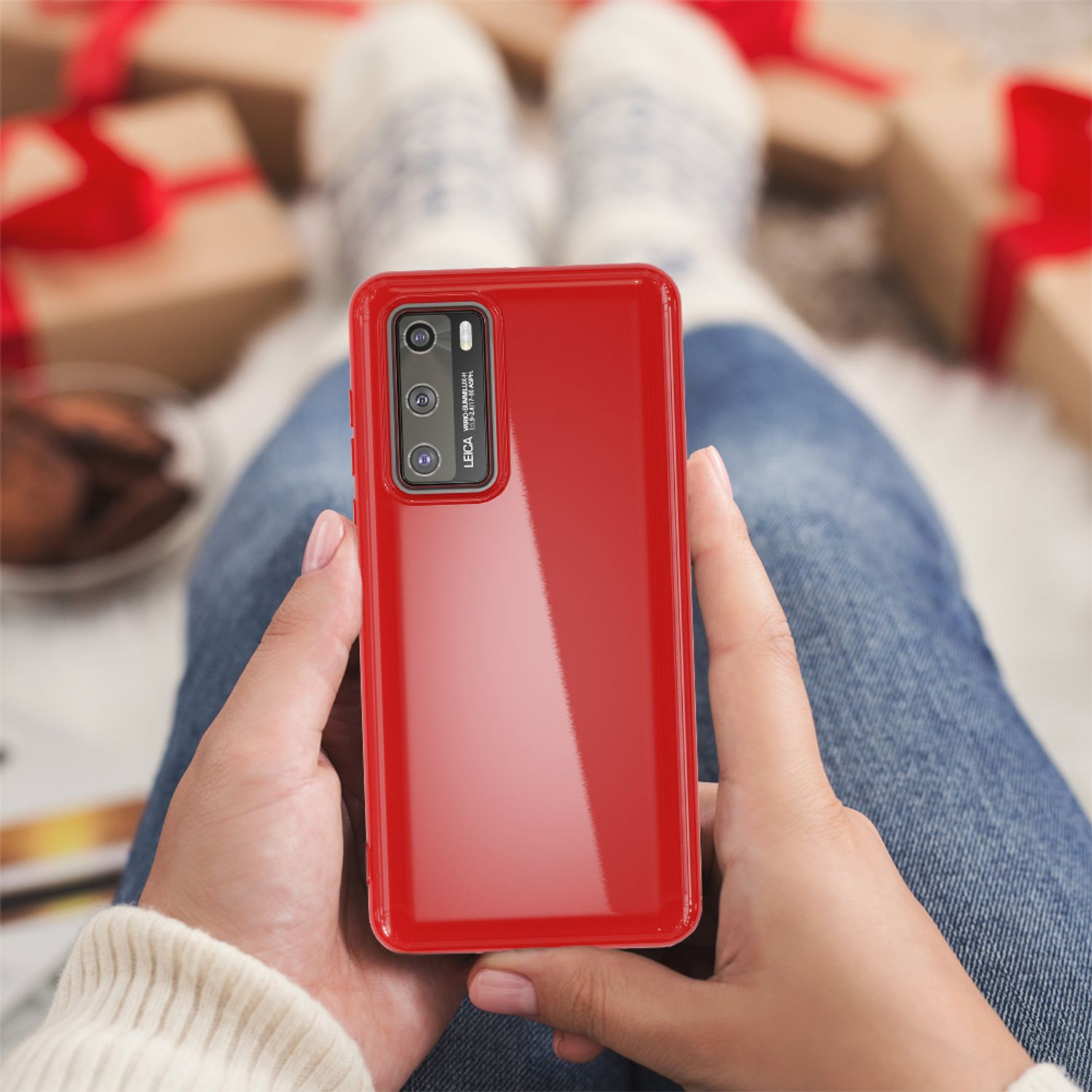 Eine Person hält ein rotes Telefon mit Hülle, während sie in einer gemütlichen Umgebung mit Geschenken sitzt und Socken trägt.
