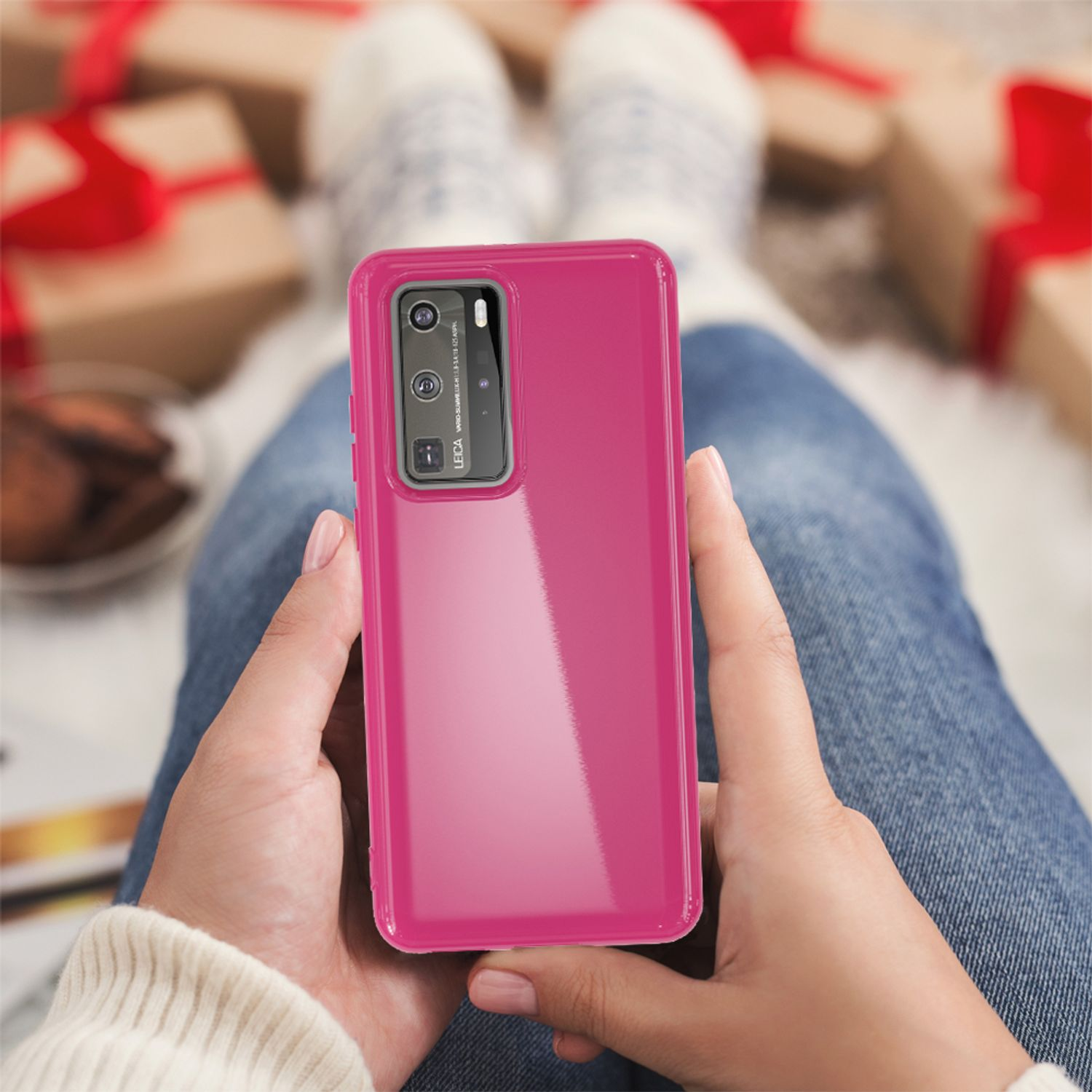 Eine Frau hält ein rosa Telefon in einer Hülle, sitzt auf einem Schoß mit Weihnachtsgeschenken.