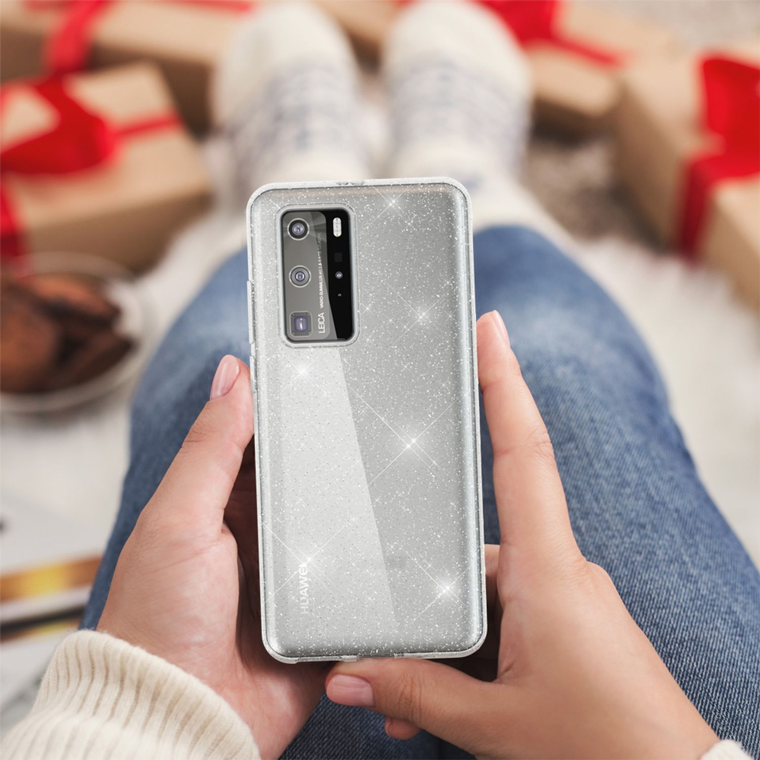 Eine Person hält ein Telefon mit glitzernder Hülle vor einem Hintergrund mit gemütlichen, festlichen Elementen.