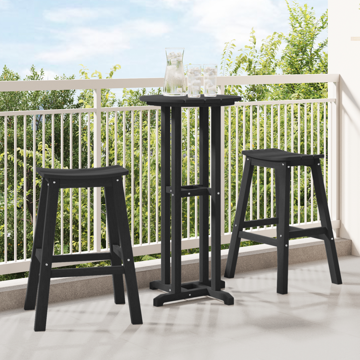 Schwarzes Outdoor-Bar-Set: Tisch, zwei Hocker und Gläser. Balkon mit Grün im Hintergrund.