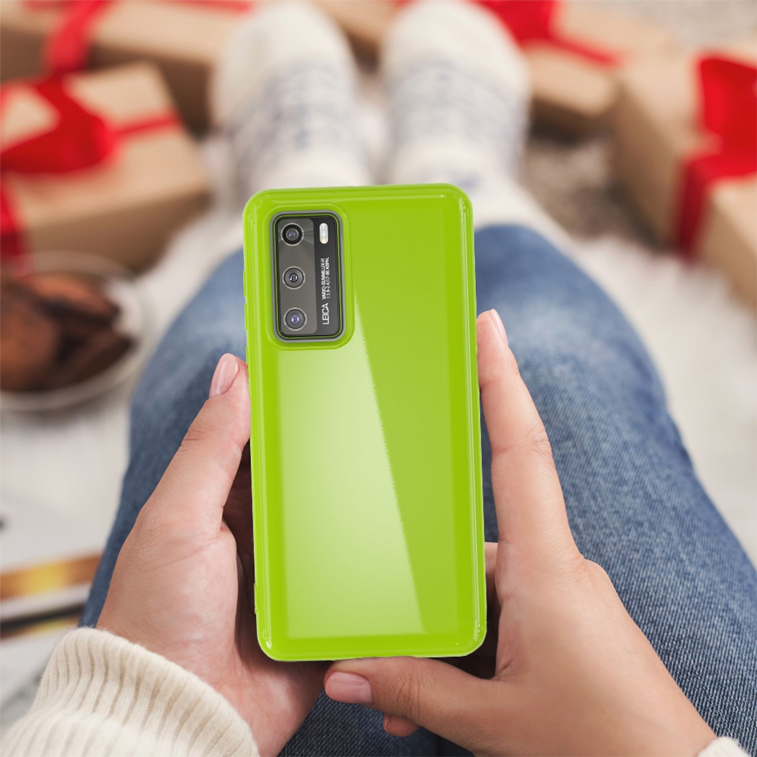 Eine Person hält ein grünes Telefon. Das Telefon hat eine Kamera und ist in einer grünen Hülle. Hintergrund Geschenke.