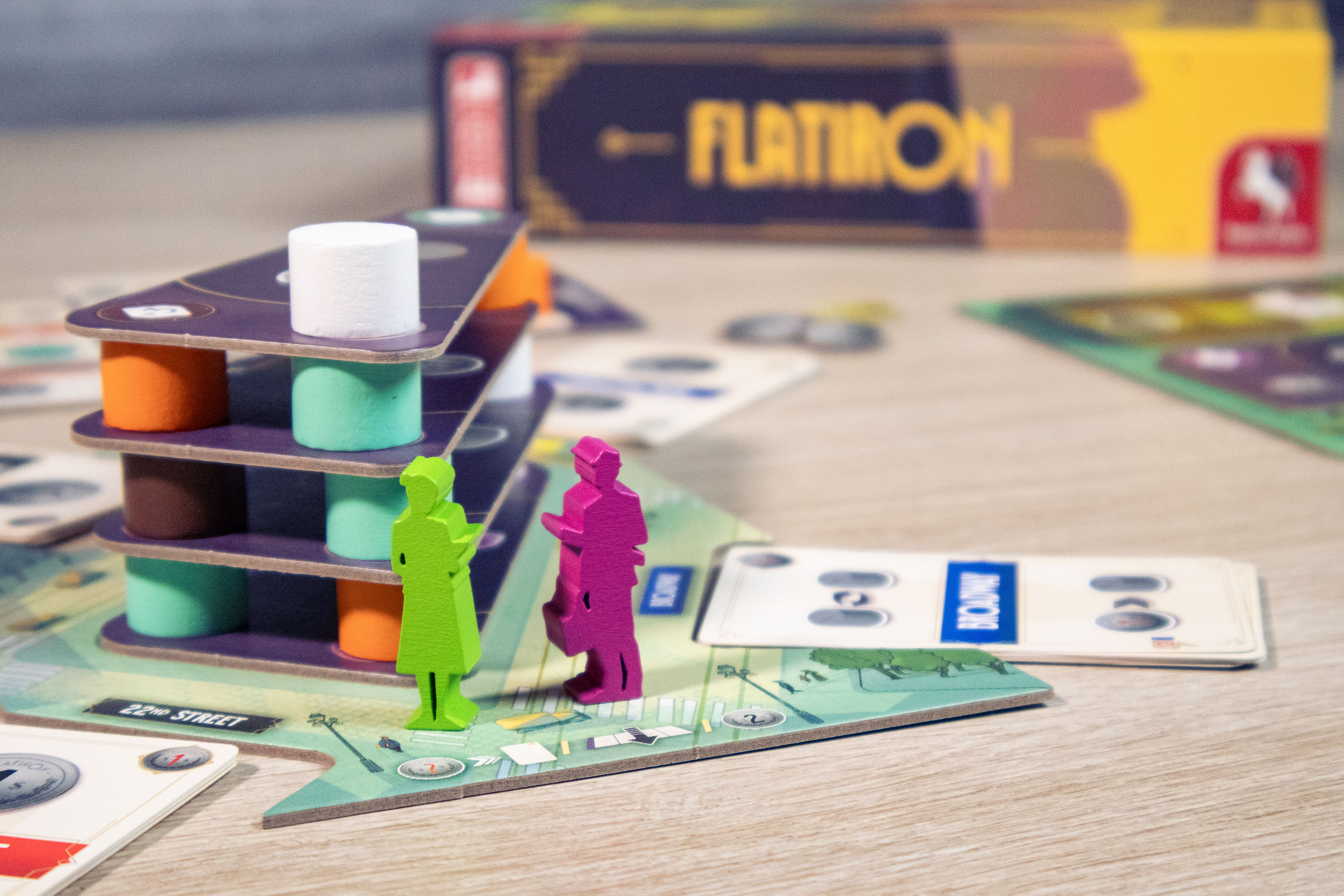 Configurazione del gioco da tavolo con miniature di edifici, pedine dei giocatori e carte su una superficie di legno.