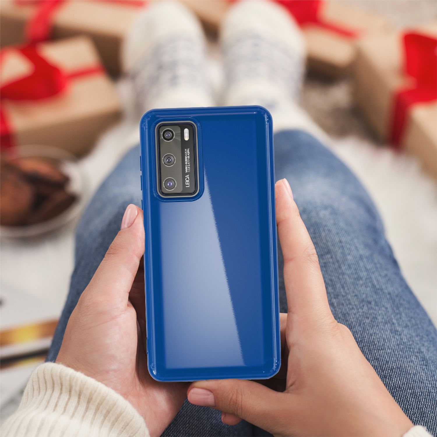 Hände, die eine blaue Handyhülle halten. Der Hintergrund umfasst Beine, Socken und Geschenke.