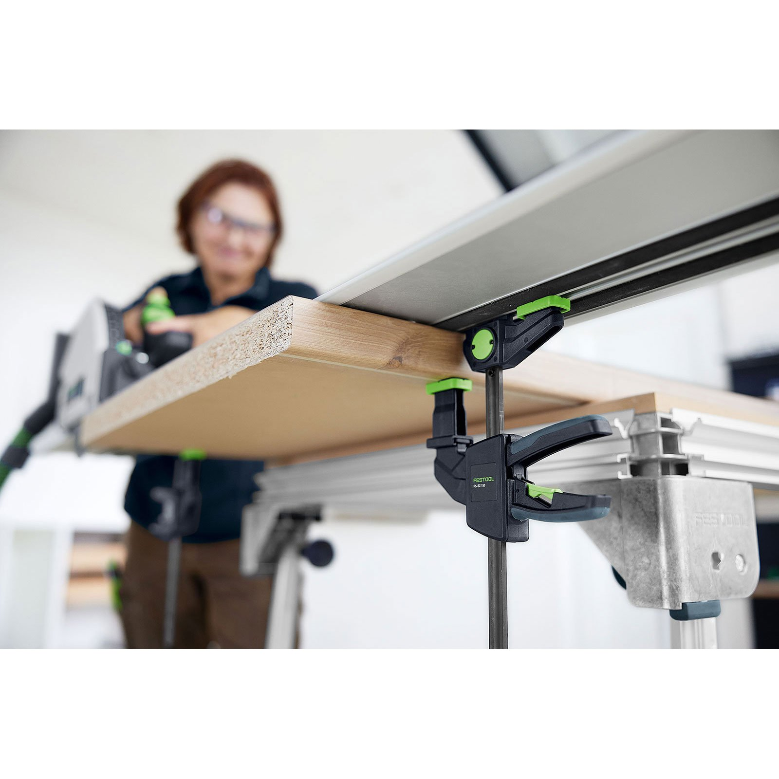 Eine Person, die eine Säge benutzt, um ein Holzstück zu schneiden, das auf einer Werkbank eingespannt ist. Eine Klemme ist sichtbar.