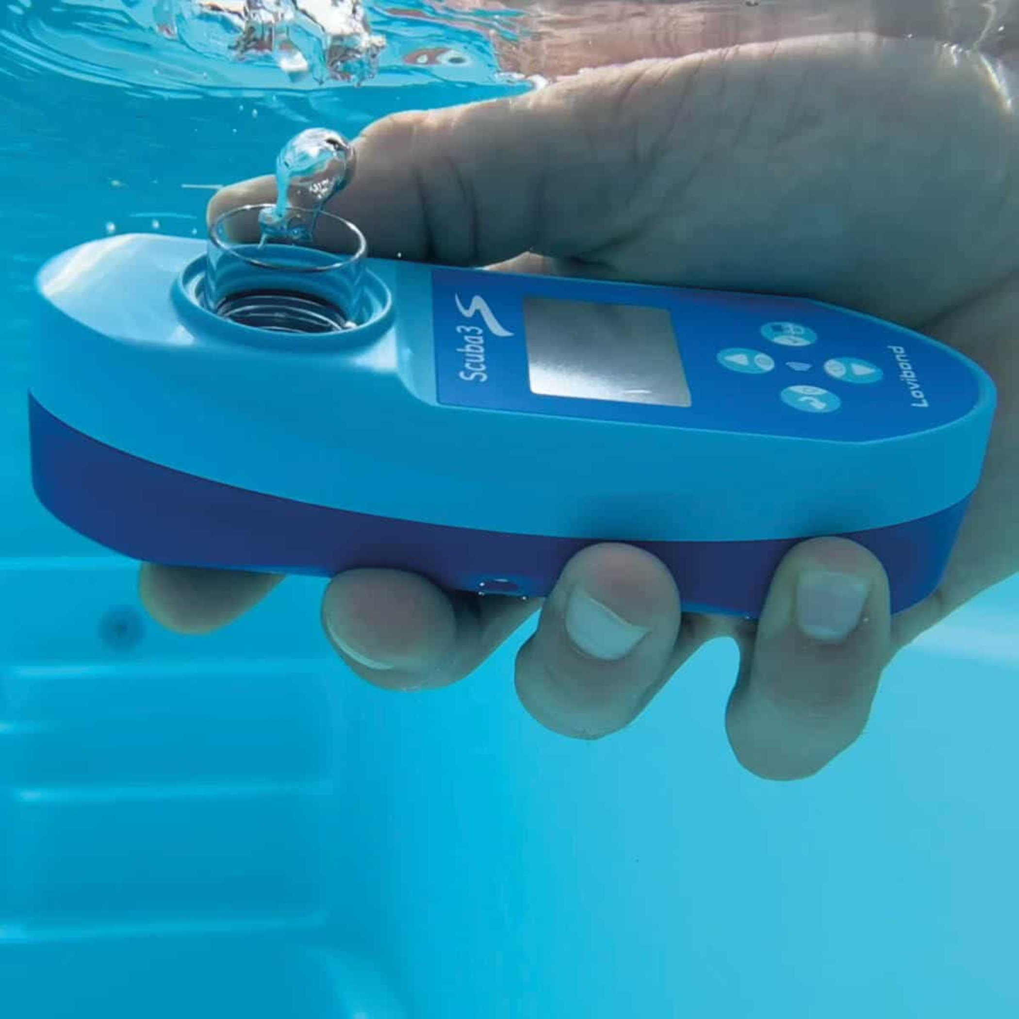 Una mano vierte líquido en un dispositivo azul para pruebas de agua. La escena es cerca de una piscina, con agua visible.