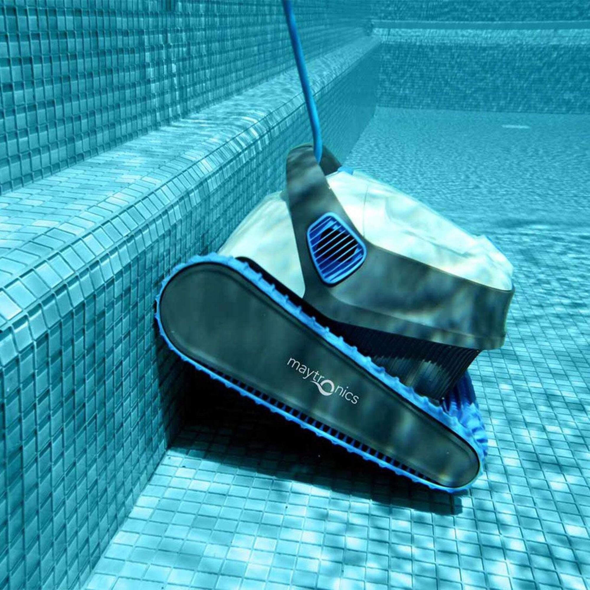 Una vista submarina de un limpiador de piscina cerca de los escalones de la piscina. Tiene orugas azules y un cuerpo gris.