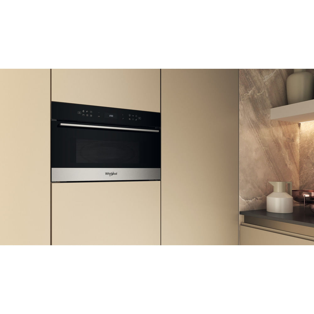 Un horno microondas Whirlpool empotrado en una pared beige, con una jarra blanca a la derecha.