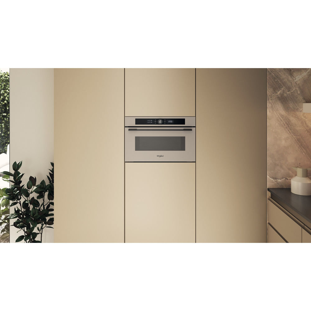 Un forno a microonde a incasso in una cucina. Il forno è installato in mobili beige con un frontale argentato.