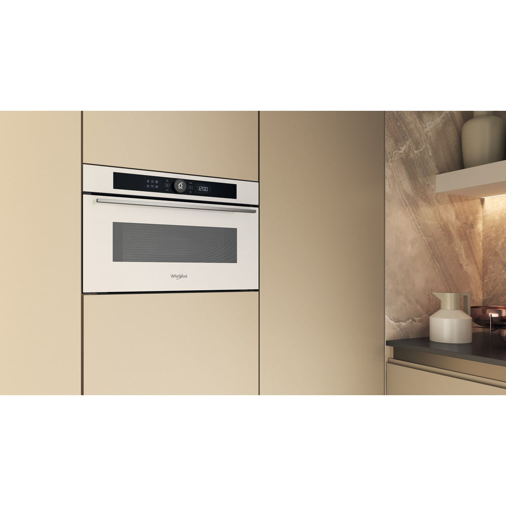 Un forno a microonde bianco è integrato in un armadio beige. Una finestra a destra.