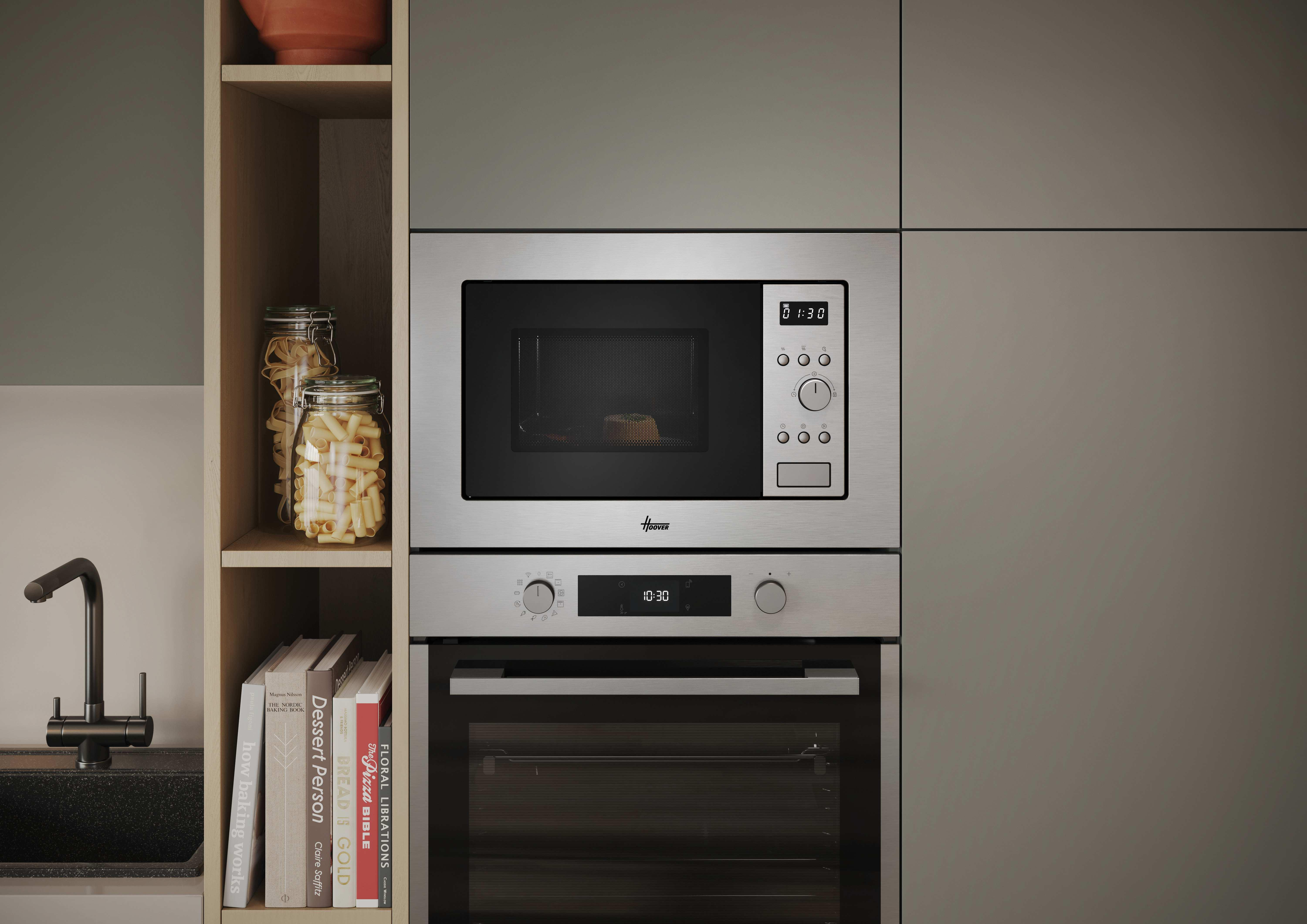 Microondas y horno de acero inoxidable. Frascos con pasta y libros en estantes. Ambiente de cocina, diseño moderno.