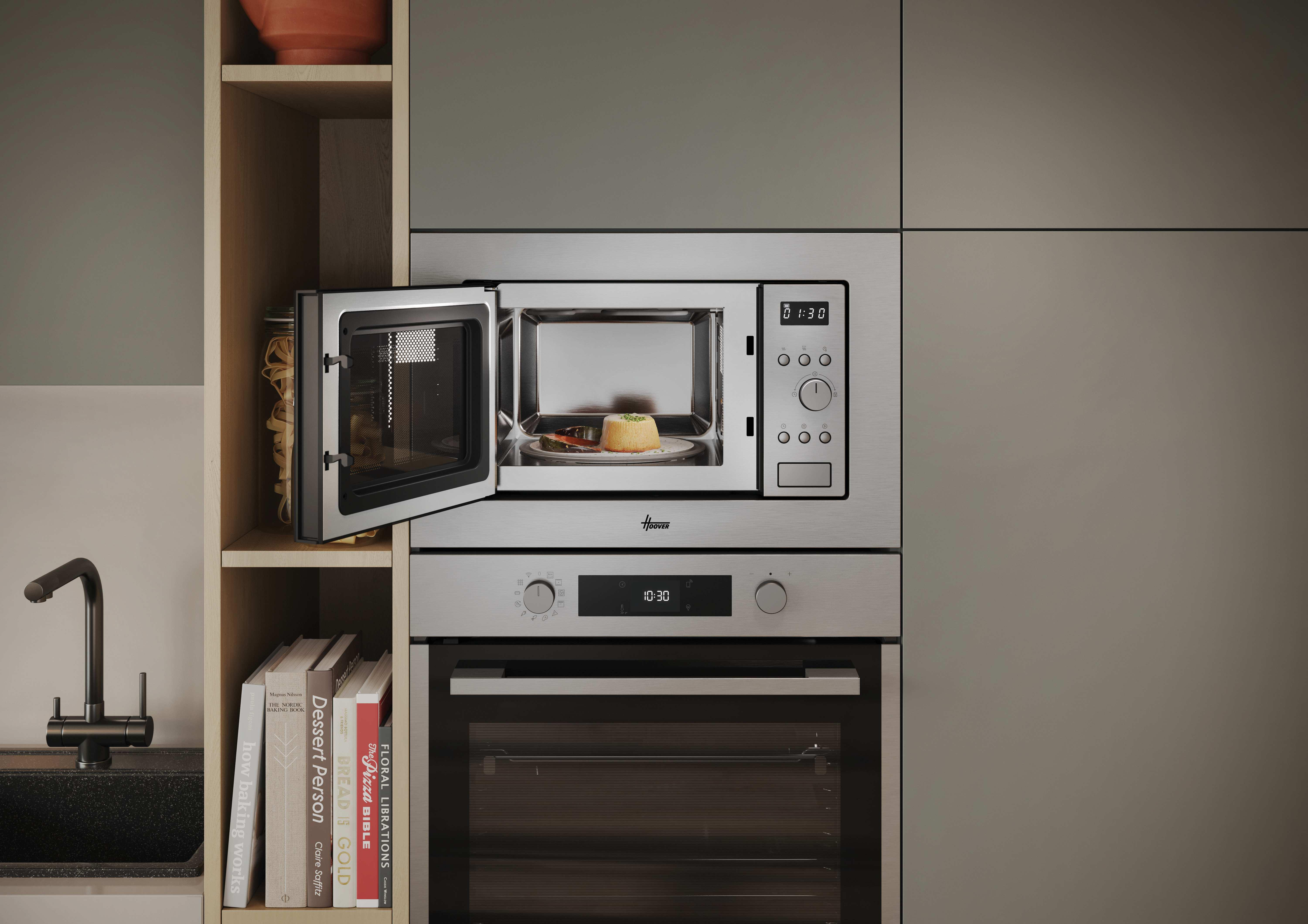 Microondas con puerta abierta. Comida dentro. Ambiente de cocina con frascos, libros y diseño moderno.