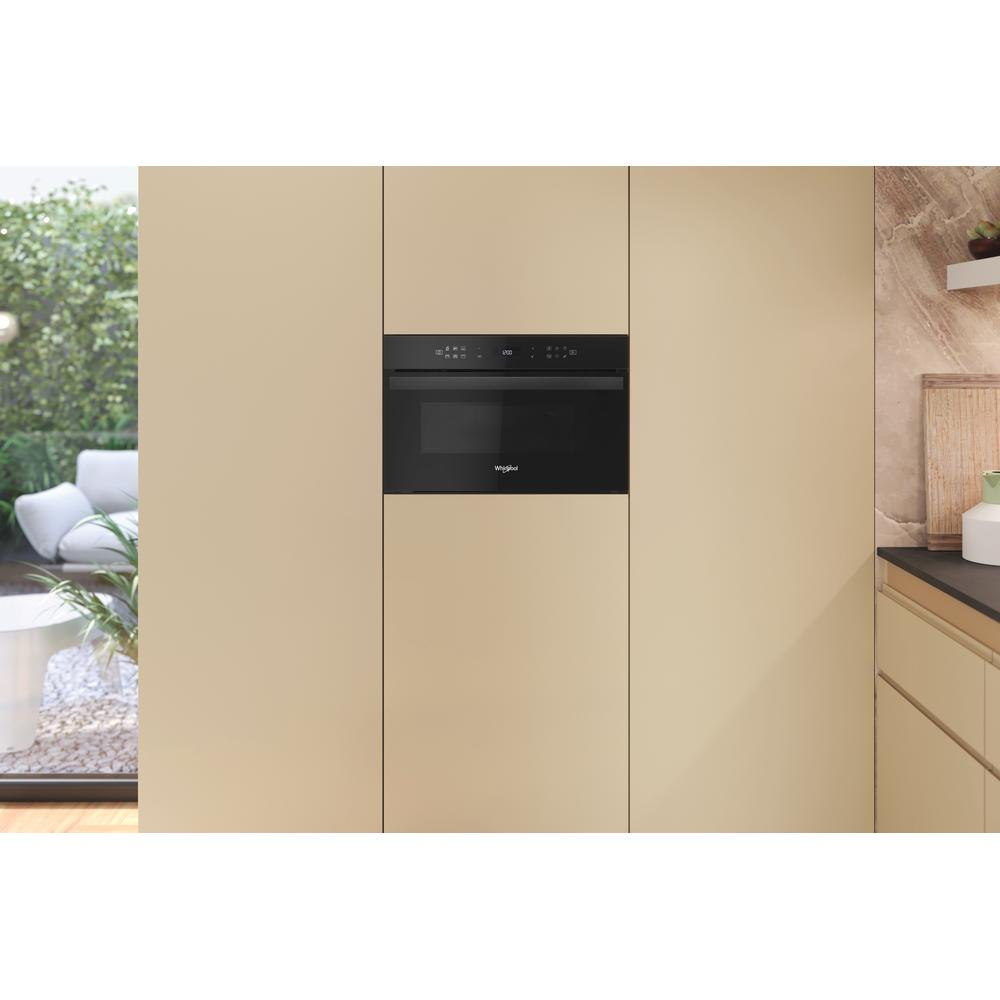 Wbudowana kuchenka mikrofalowa w beżowej kuchni, z widokiem na zieloną scenerię na zewnątrz.