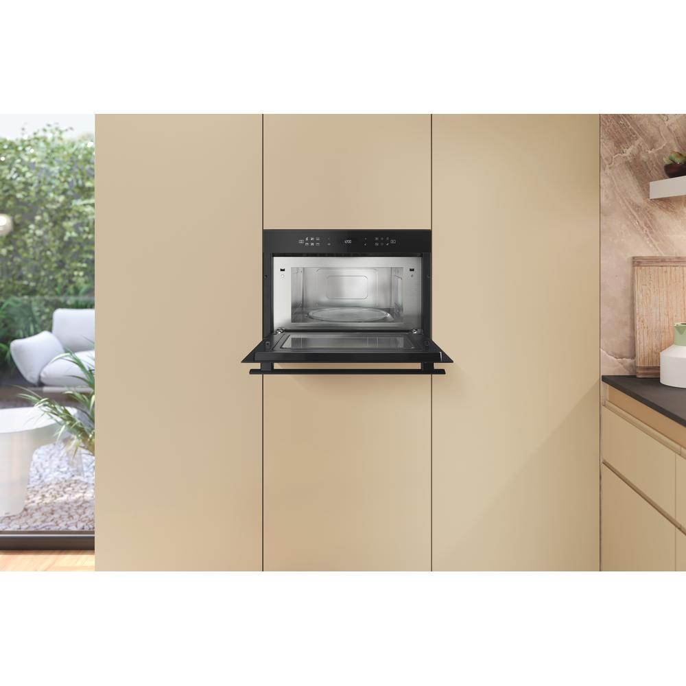 Wbudowana kuchenka mikrofalowa w beżowej kuchni. Drzwi są otwarte, pokazując wnętrze.