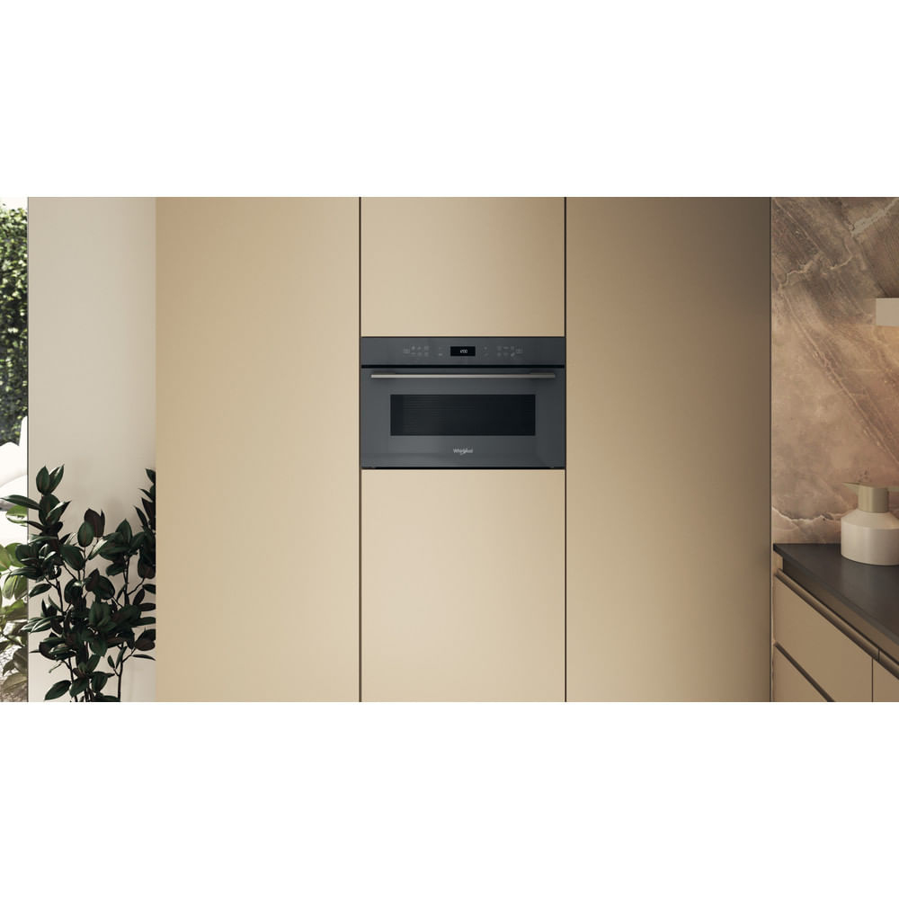 A black microwave oven in a beige kitchen. The oven is built into the wall. A plant is in the foreground.