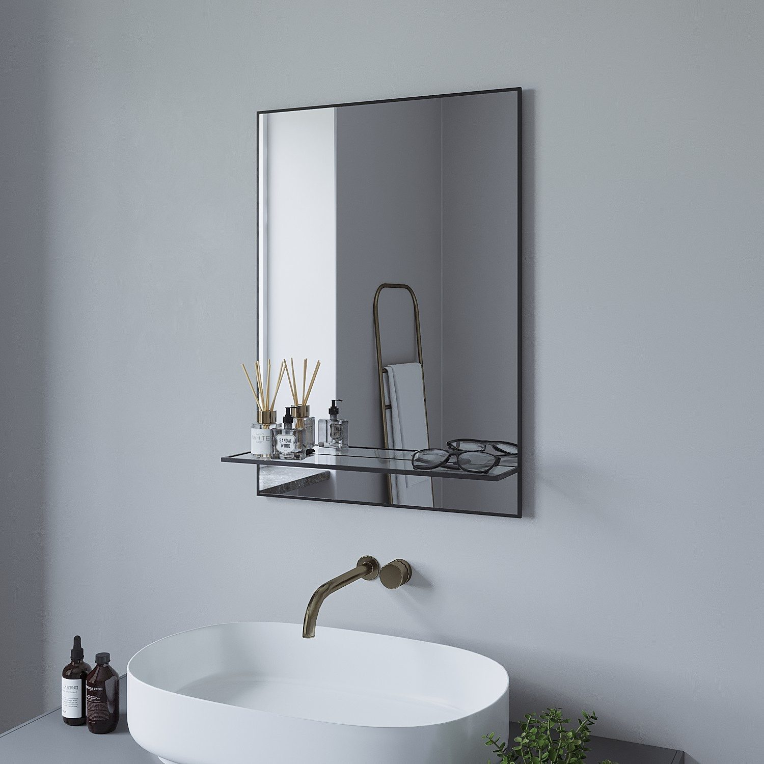 Ein Badezimmerspiegel mit schwarzem Rahmen und Regal. Verfügt über ein Waschbecken, Zubehör und einen Blick auf den Raum.