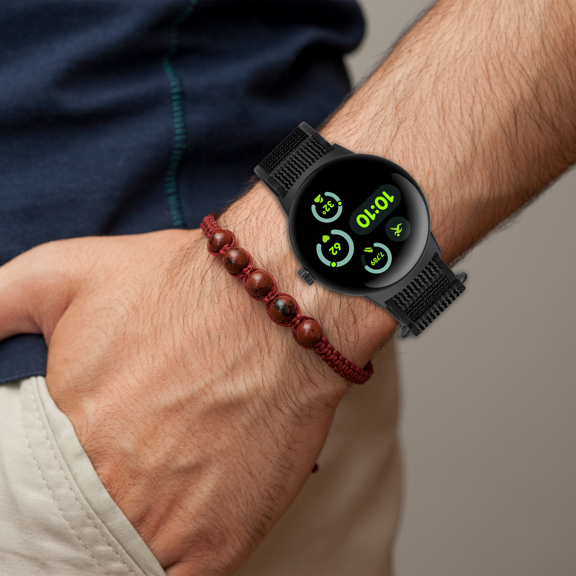 Das Handgelenk einer Person mit einer schwarzen Smartwatch und einem roten Perlenarmband.