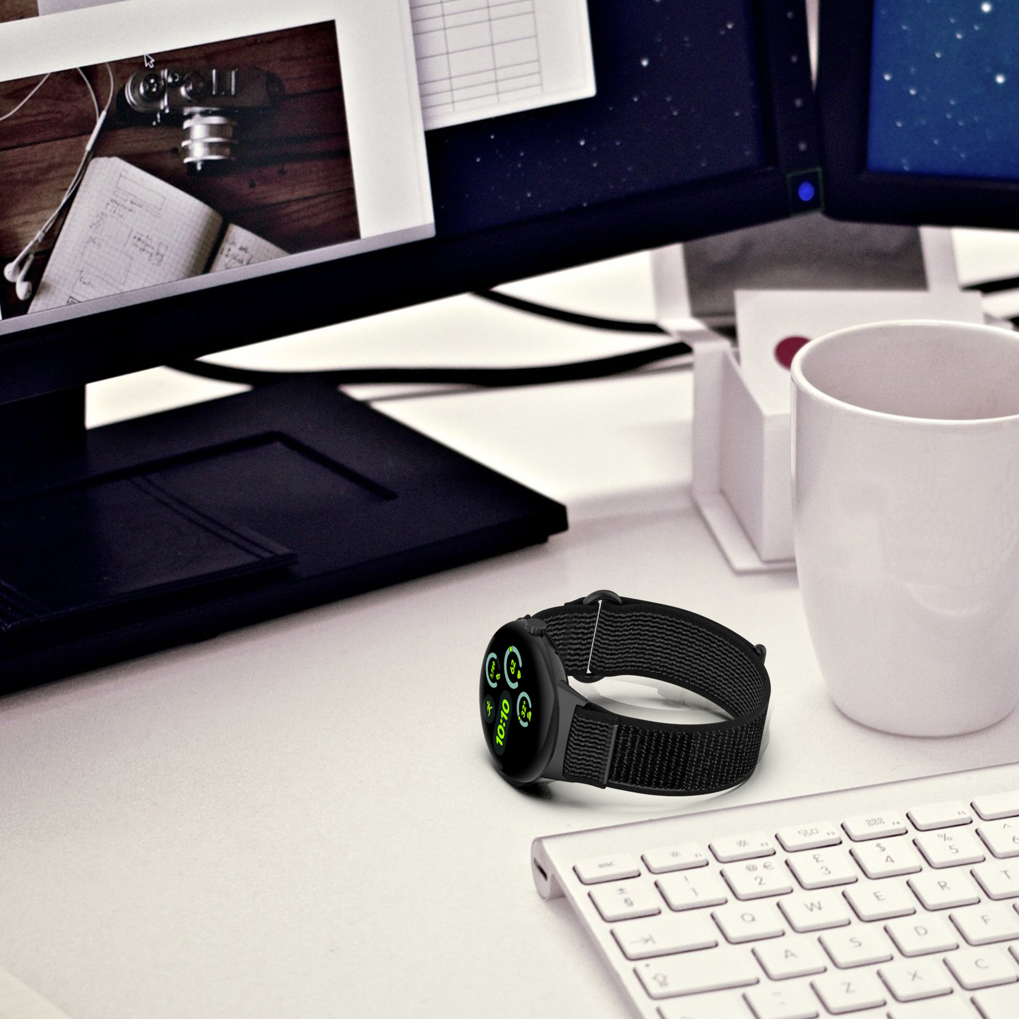 Eine schwarze Smartwatch mit grünem Display auf einem weißen Schreibtisch, in der Nähe von Tastatur und Monitoren.