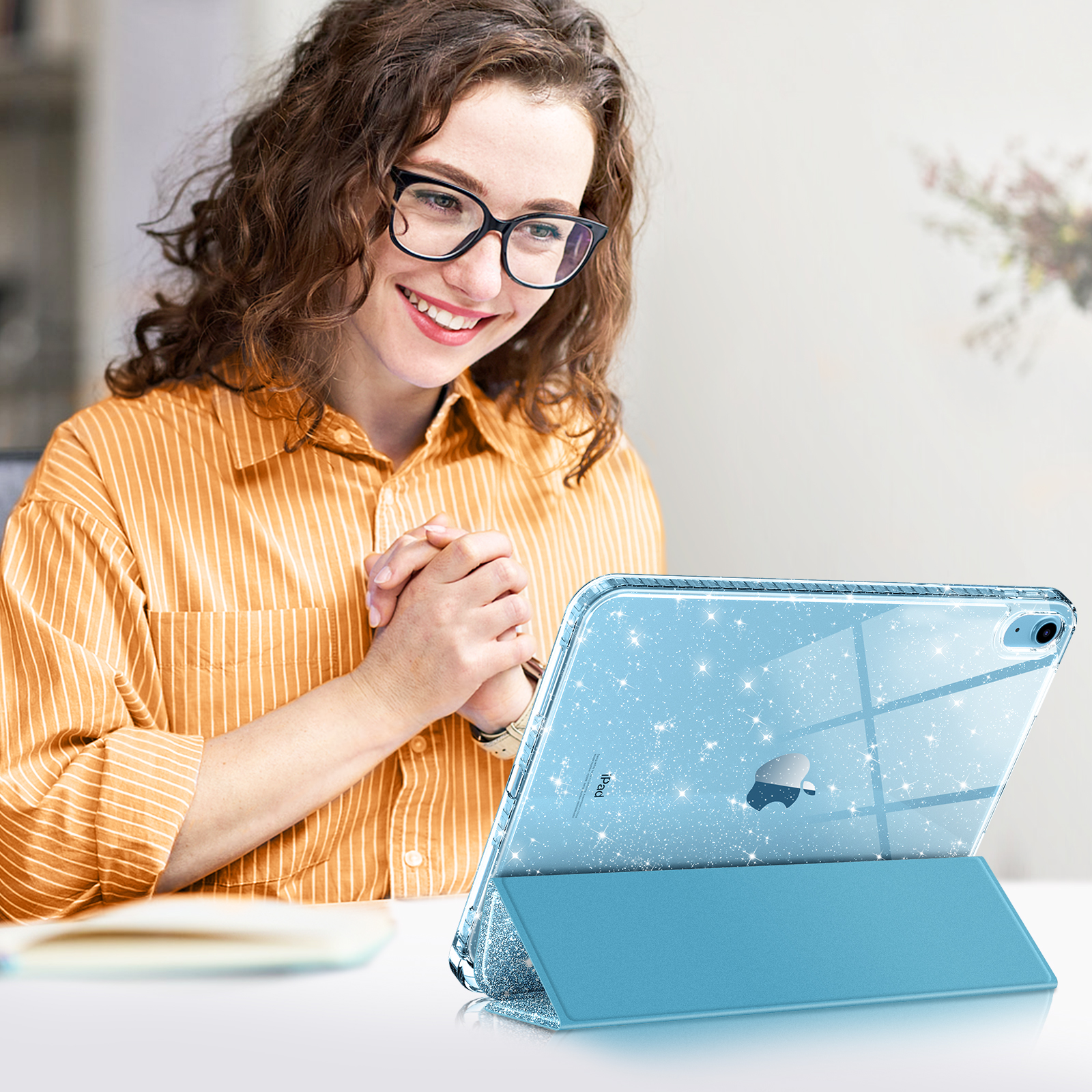 Eine lächelnde Frau benutzt ein Tablet. Das Tablet steht in einem Ständer und hat eine blaue Glitzerhülle.