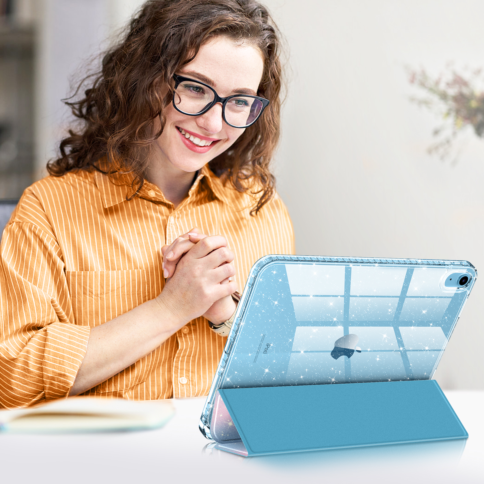 Frau mit Brille lächelt, während sie ein iPad benutzt. Das iPad ist in einer Ständerhülle mit blauem Cover.
