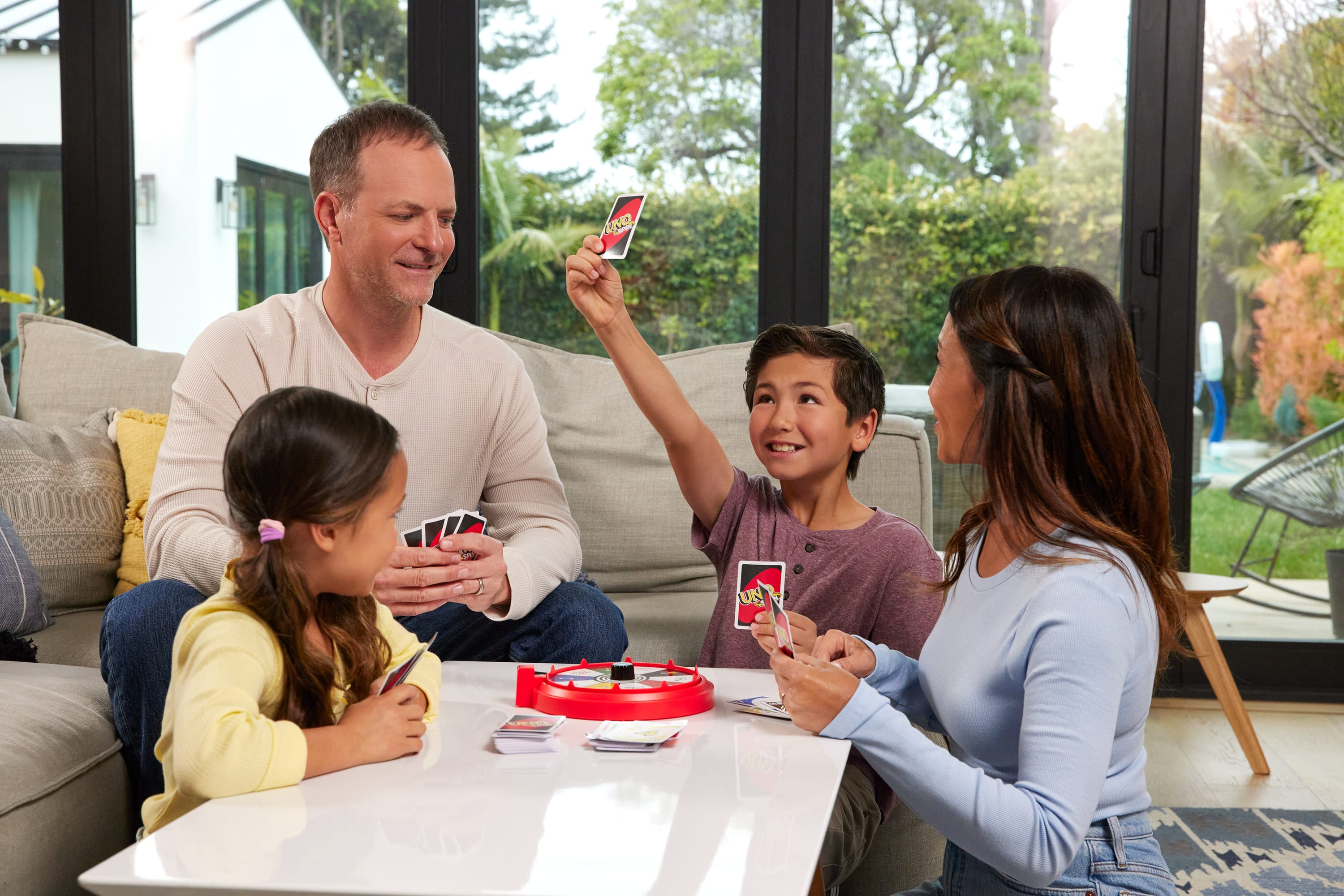 Une famille joue au Uno. Un garçon lève une carte Uno, tandis que d'autres tiennent des cartes à une table.