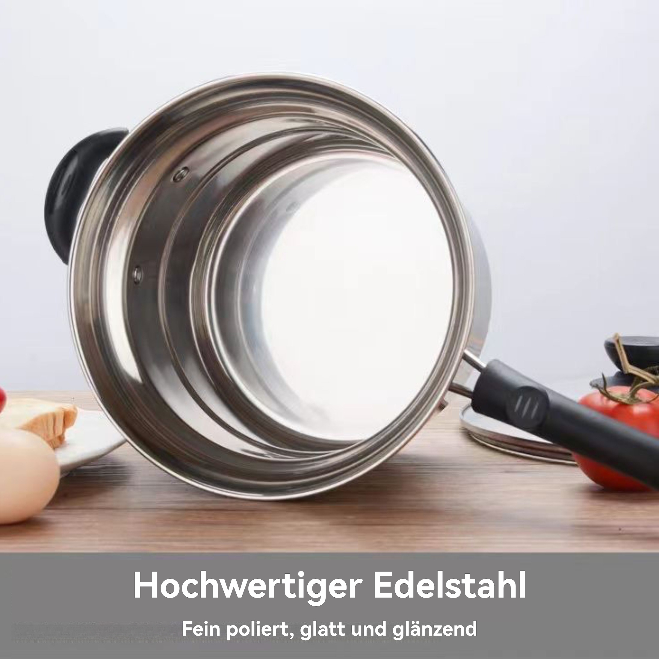 Nahaufnahme eines Edelstahltopfs mit schwarzem Griff. Zwei Tomaten liegen neben dem Griff auf der Holzoberfläche.