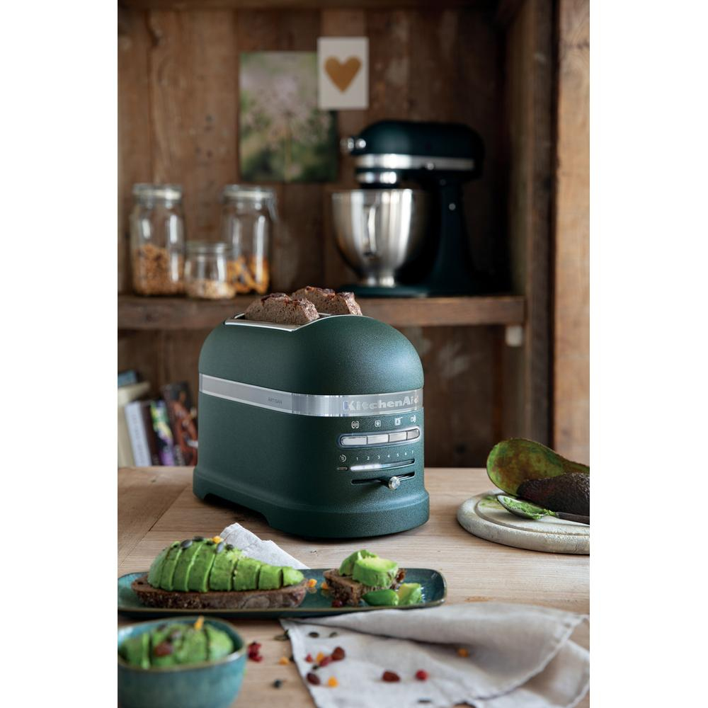 Tostapane KitchenAid verde con toast. Toast di avocado e altri elementi sono presenti. Sfondo in legno.
