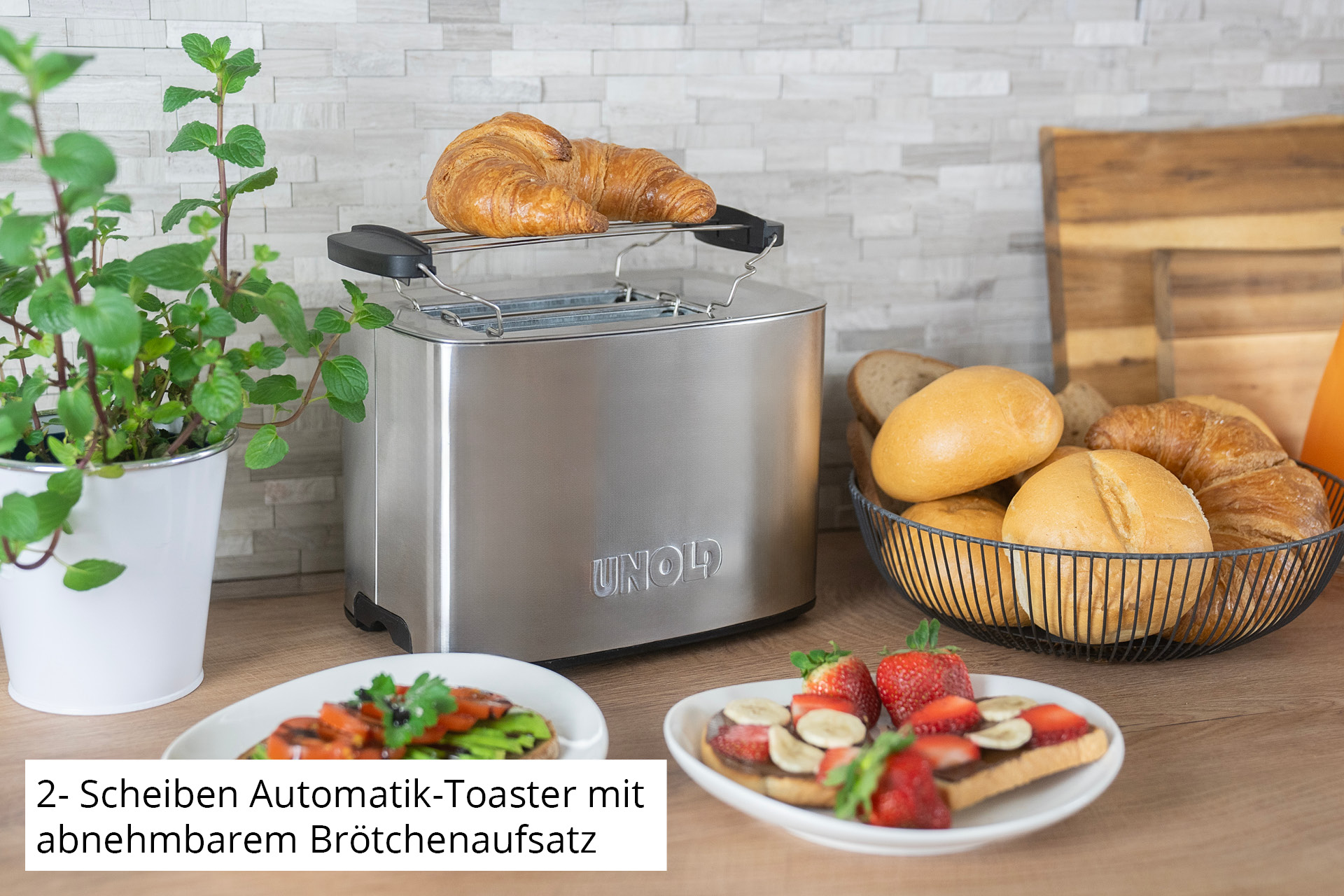 Toster ze stali nierdzewnej z rogalikiem na górze. Inne produkty spożywcze w pobliżu.