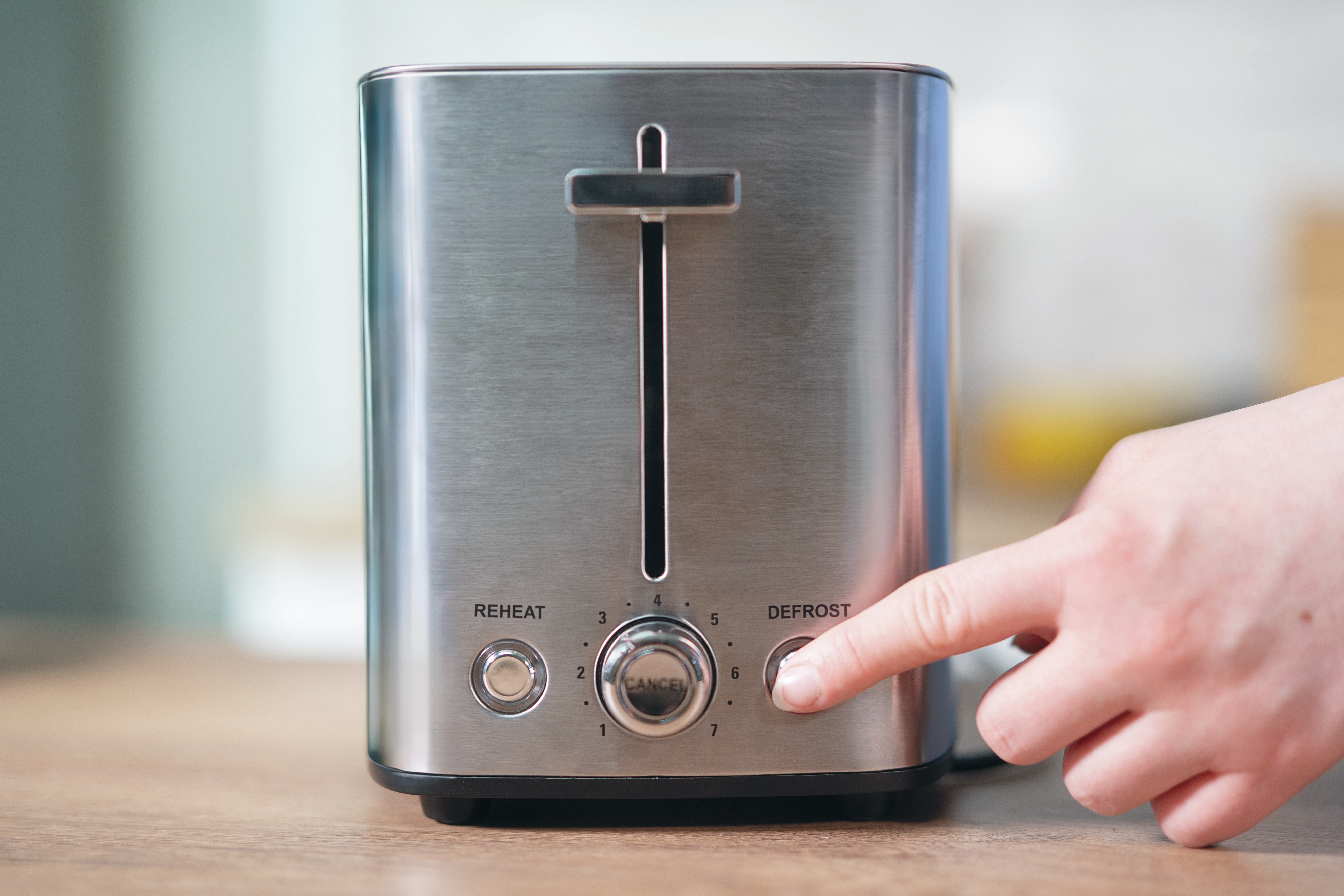 Ręka naciskająca przycisk rozmrażania w tosterze ze stali nierdzewnej.