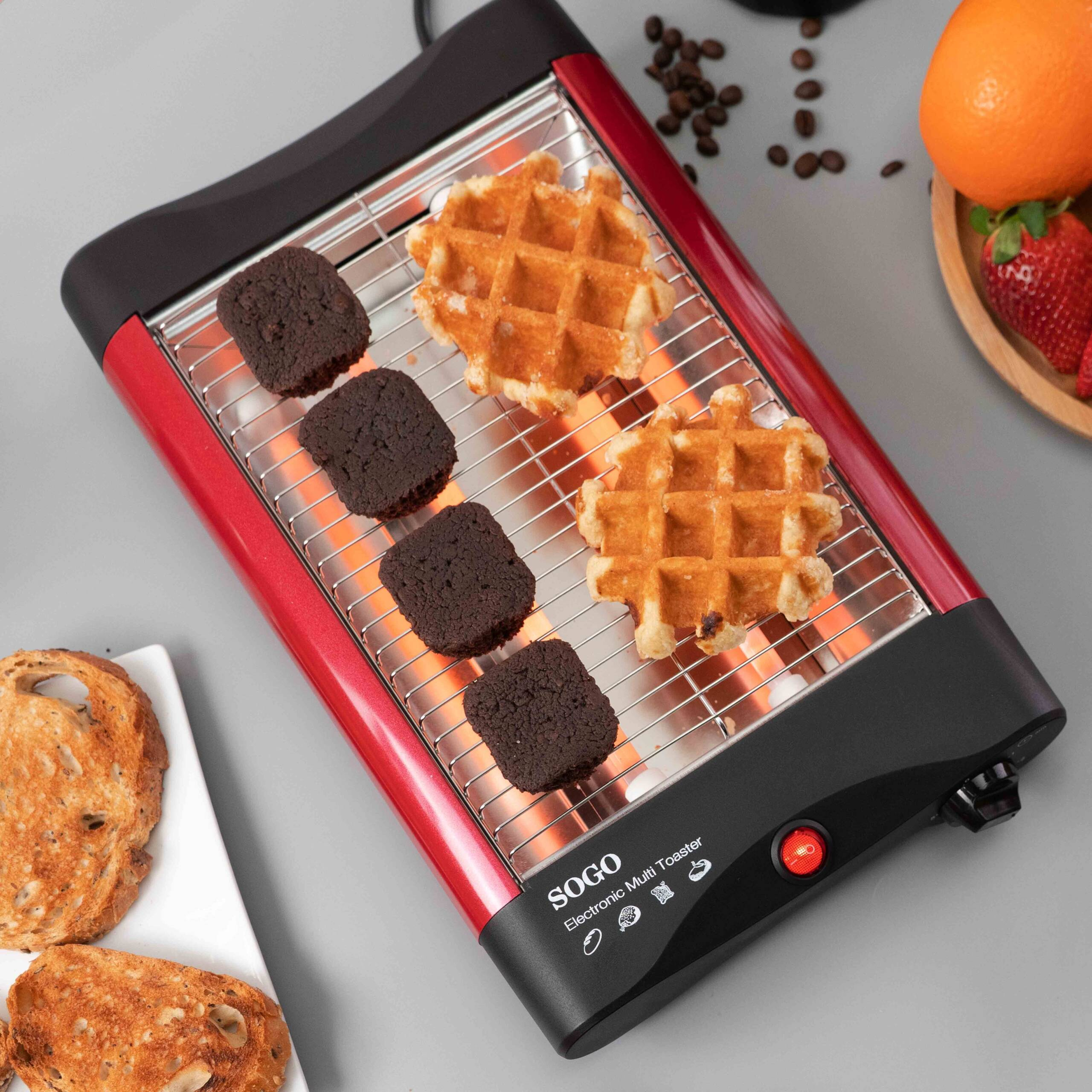 Tostapane rosso con waffle e brownies. Un piatto con pane tostato e un piatto con fragole sono a lato.