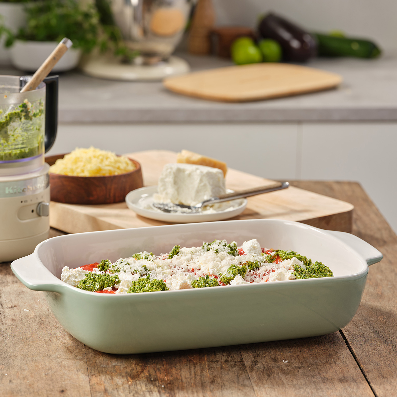 Gericht mit grünem Rand, gefüllt mit einem geschichteten Essen. Enthält Pesto, Käse und andere Zutaten.