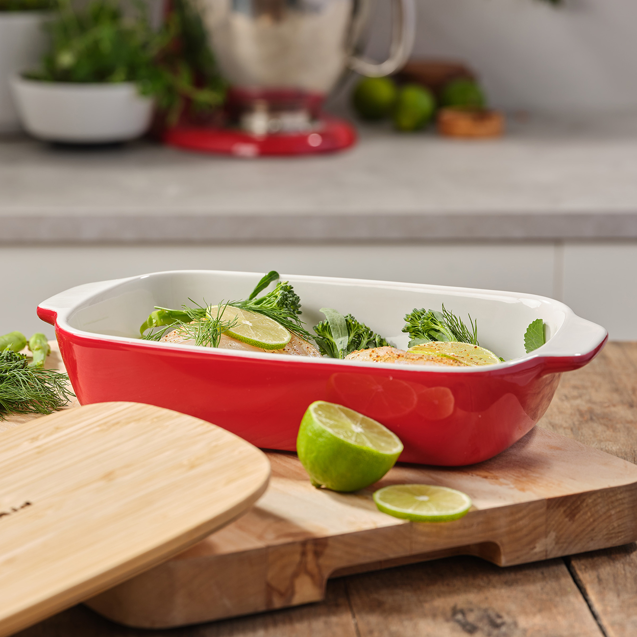 Eine rote Backform mit Essen und Limettenscheiben darauf. Ein Holzschneidebrett und eine Limettenhälfte sind vorhanden.