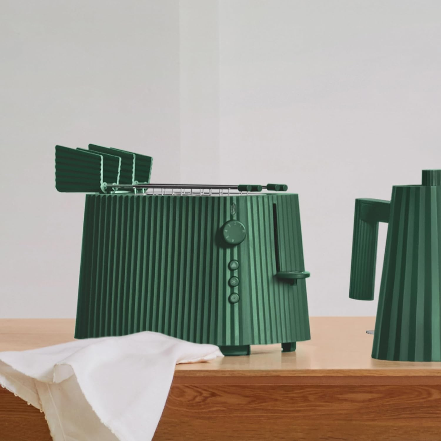 Tostapane verde a coste e bollitore abbinato su una superficie in legno, con un panno bianco davanti.